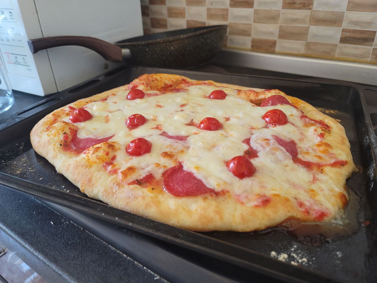 fresh pizza on the oven pan with mozzarella cheese, italian sausage, tomato sauce and cherry tomatoes