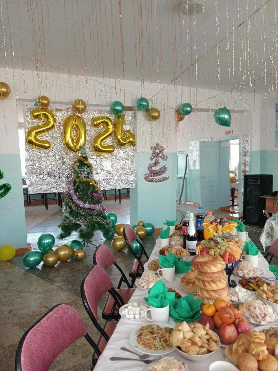 table set with a lot of food; Christmas tree in the background and gold and green balloons on the wall, including big 2 0 2 4 number balloons