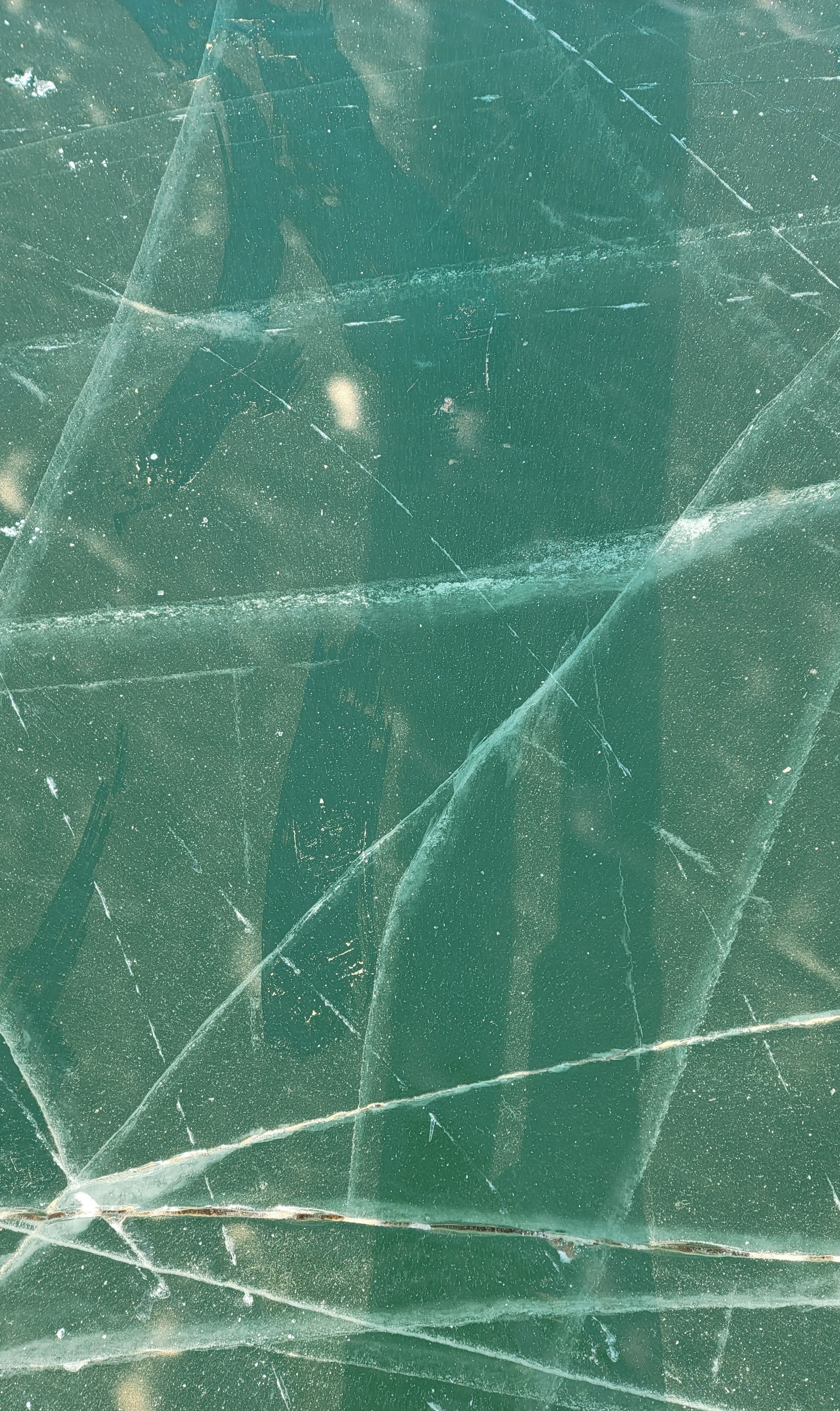 ice with ski mark cracks running through it; teal water underneath