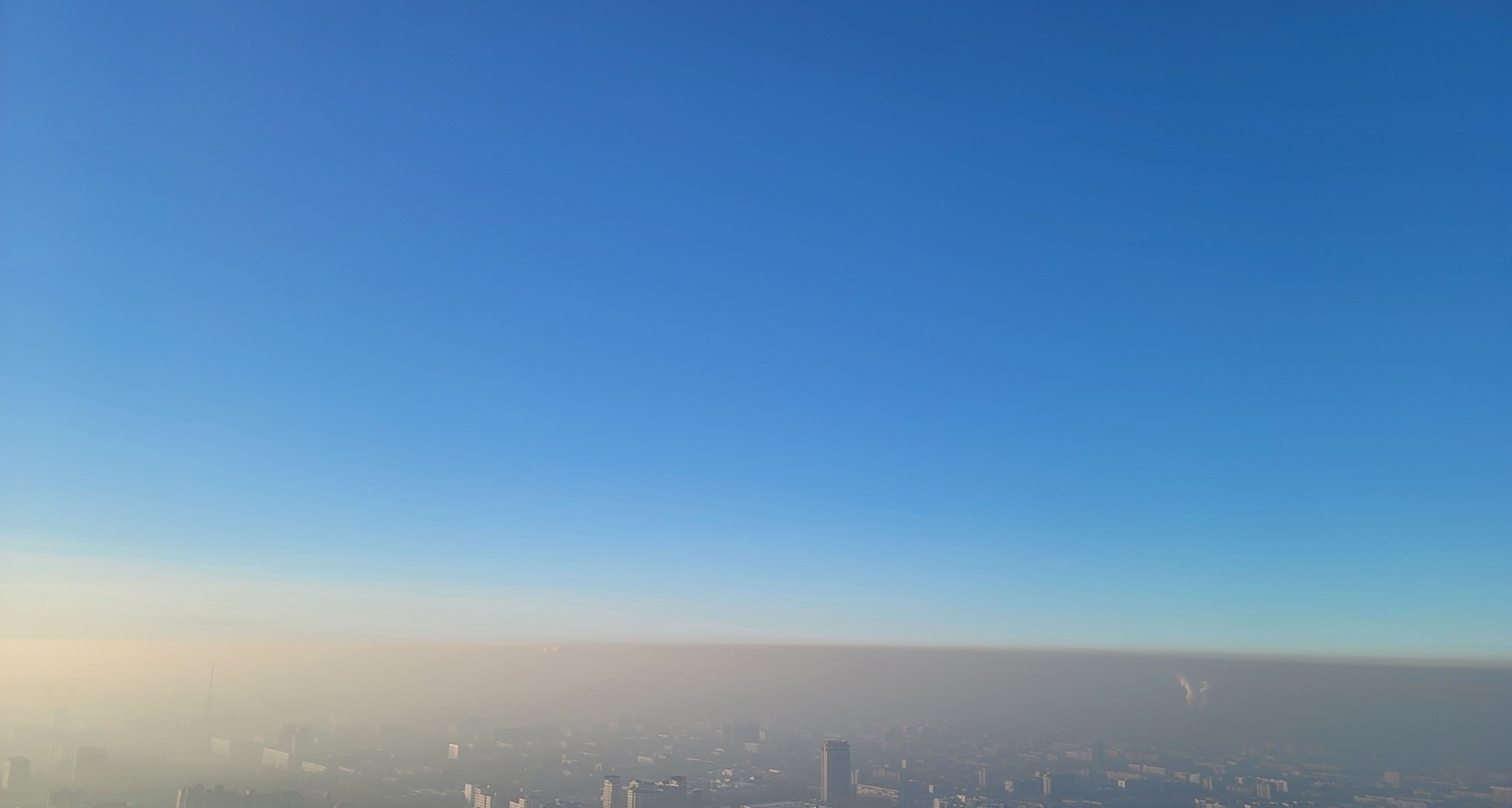 bottom fourth of the picture covered by a gray haze with city buildings barely visible; above, a blue sky