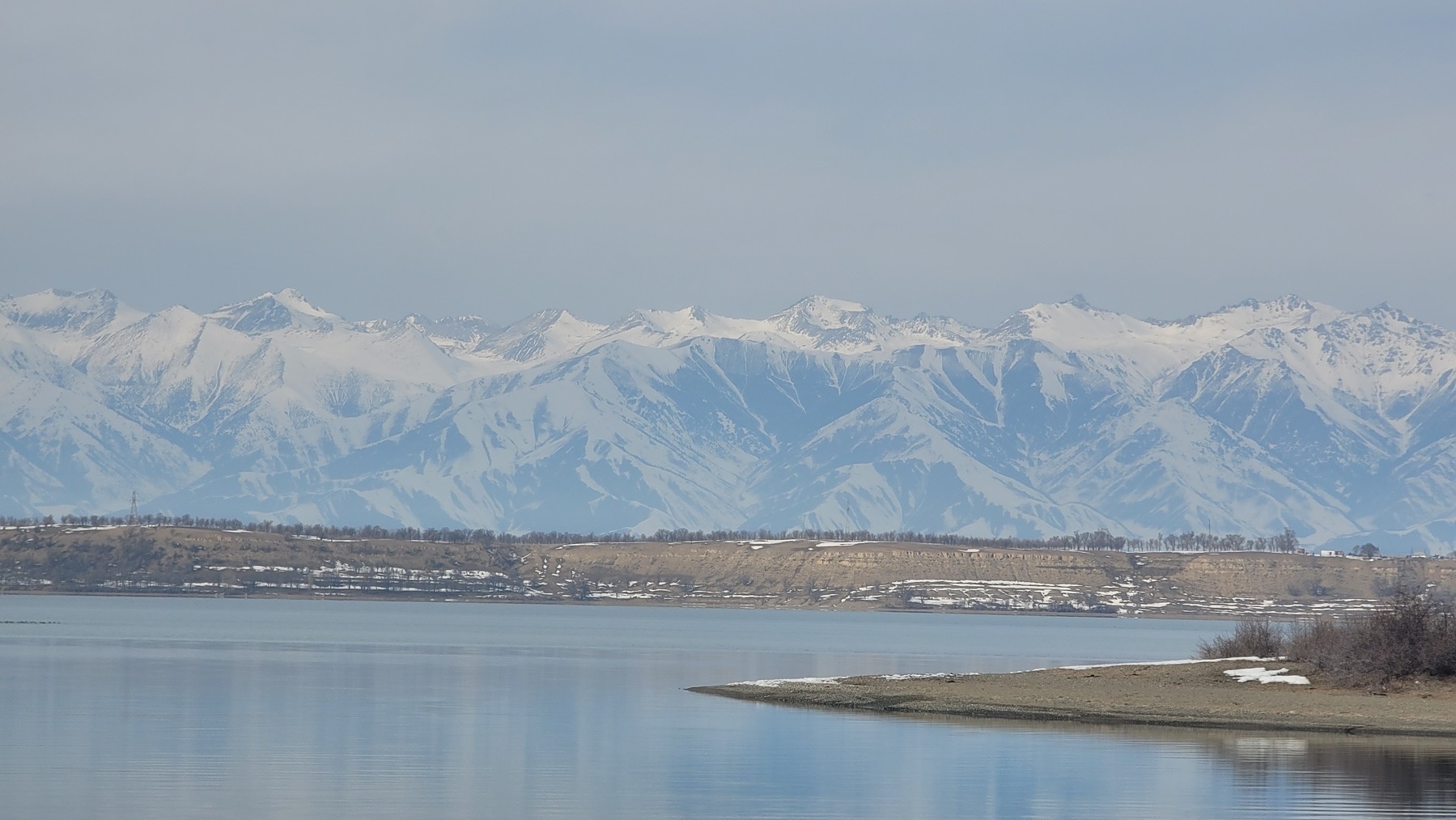 light gray-blue lake next to a brown shore with snow-capped mountains in the background