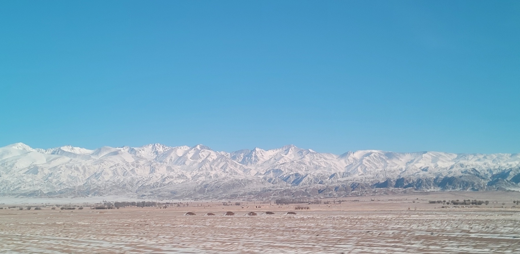 white mountains in front of a brown field with splotches of white snow