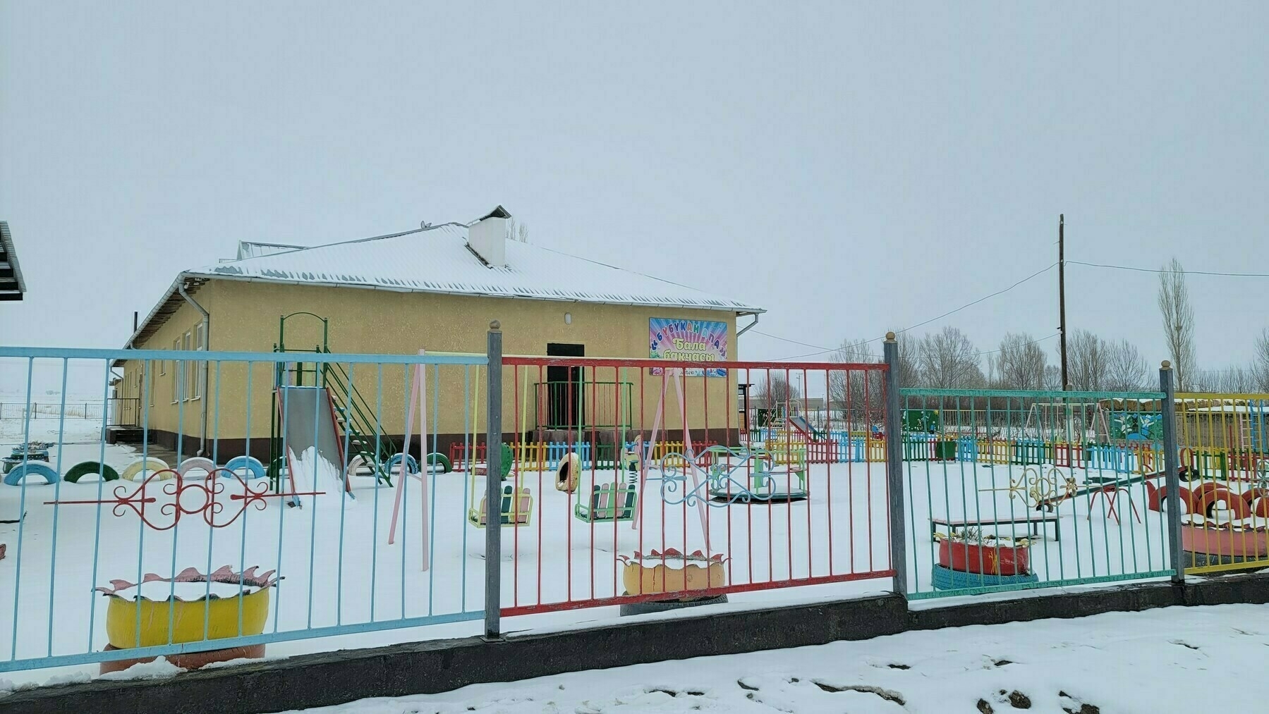 yellow building behind a colored fence with snow all around