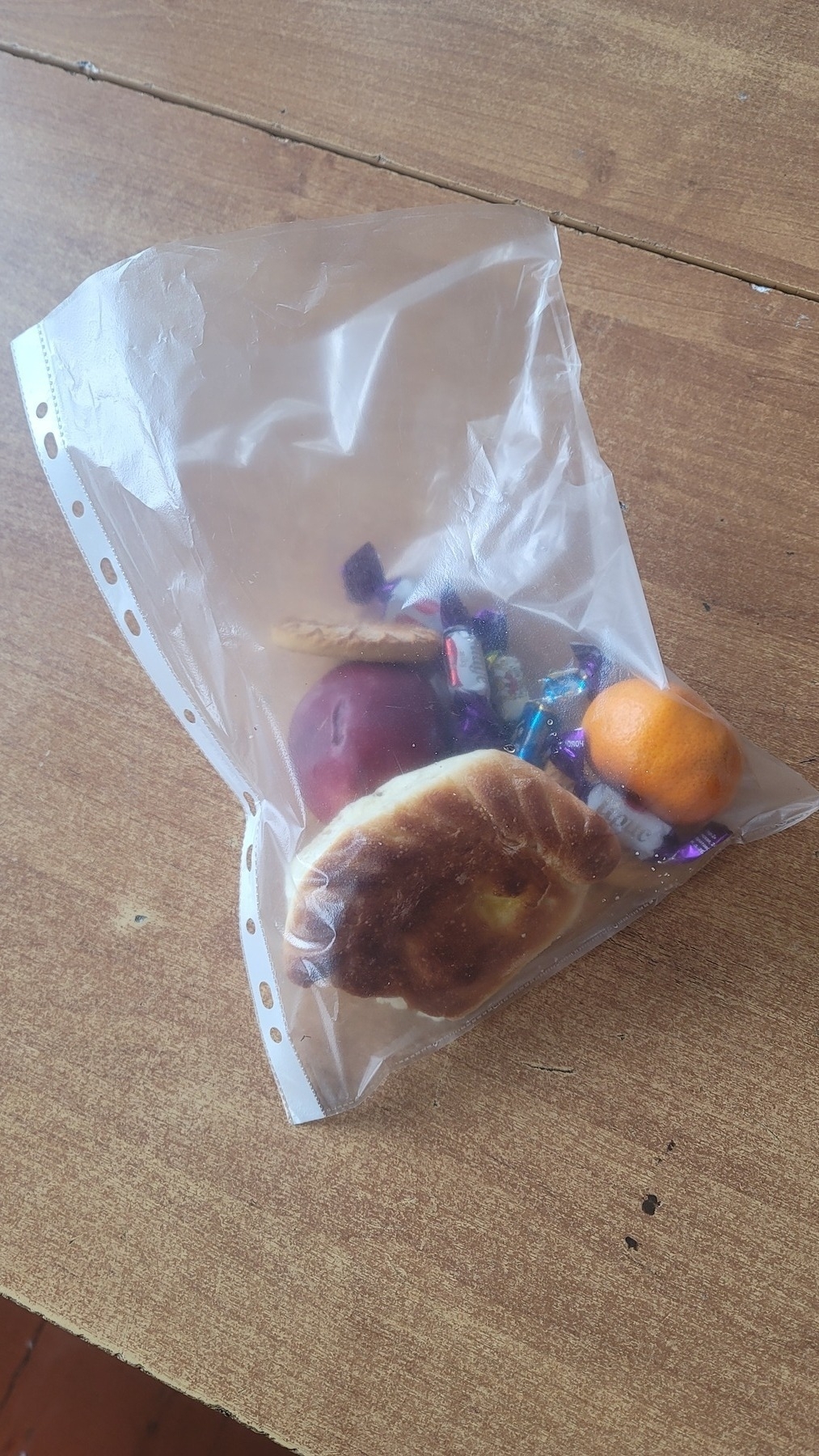 bread bun with potato filling, apple, tangerine and candies inside a plastic sheet protector