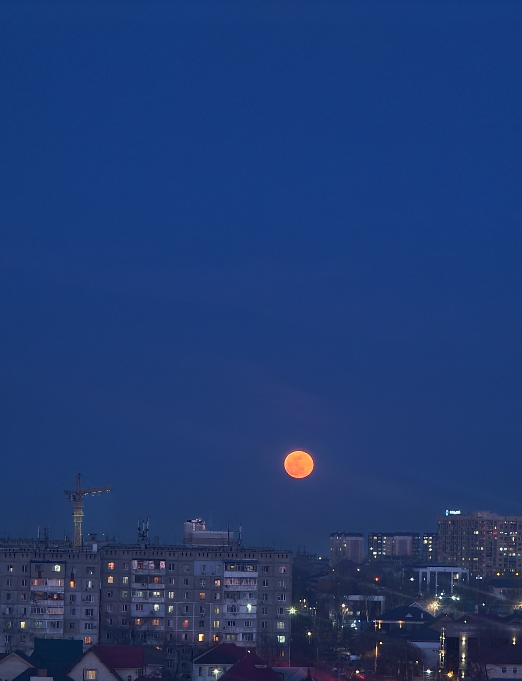 orange moon in a dark blue sky over buildings