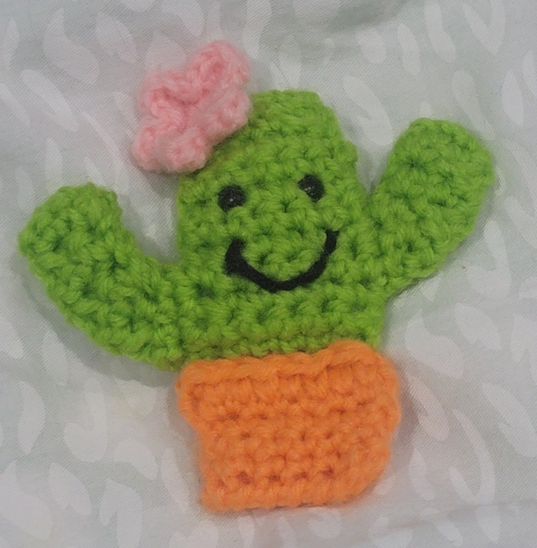 crocheted cactus in a pot with a pink flower on the top left of its head