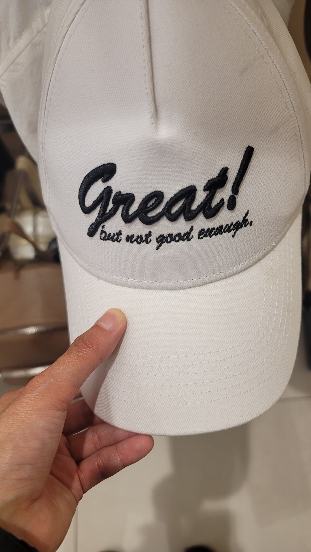 white cap with black embroidered cursive text that reads, "Great! but not good enough"