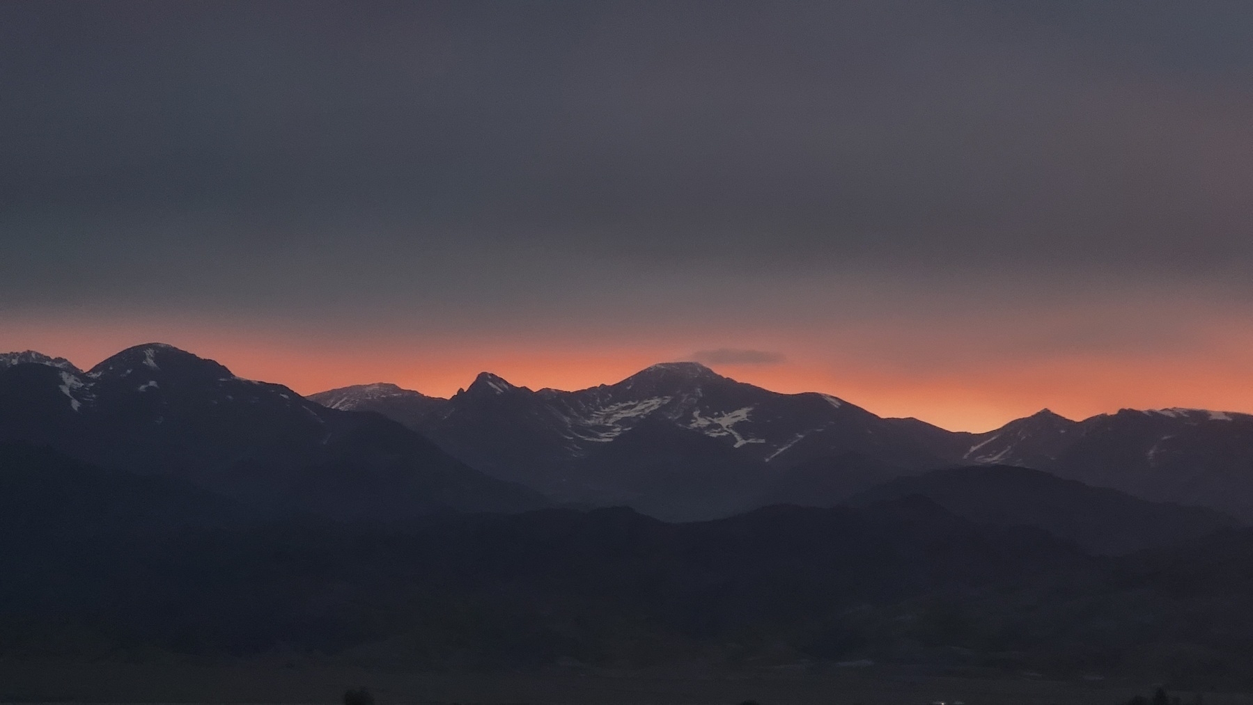 dark mountains with a little bit of snow on them; pink/orange outline of sky above the mountain peaks, dark gray sky above that