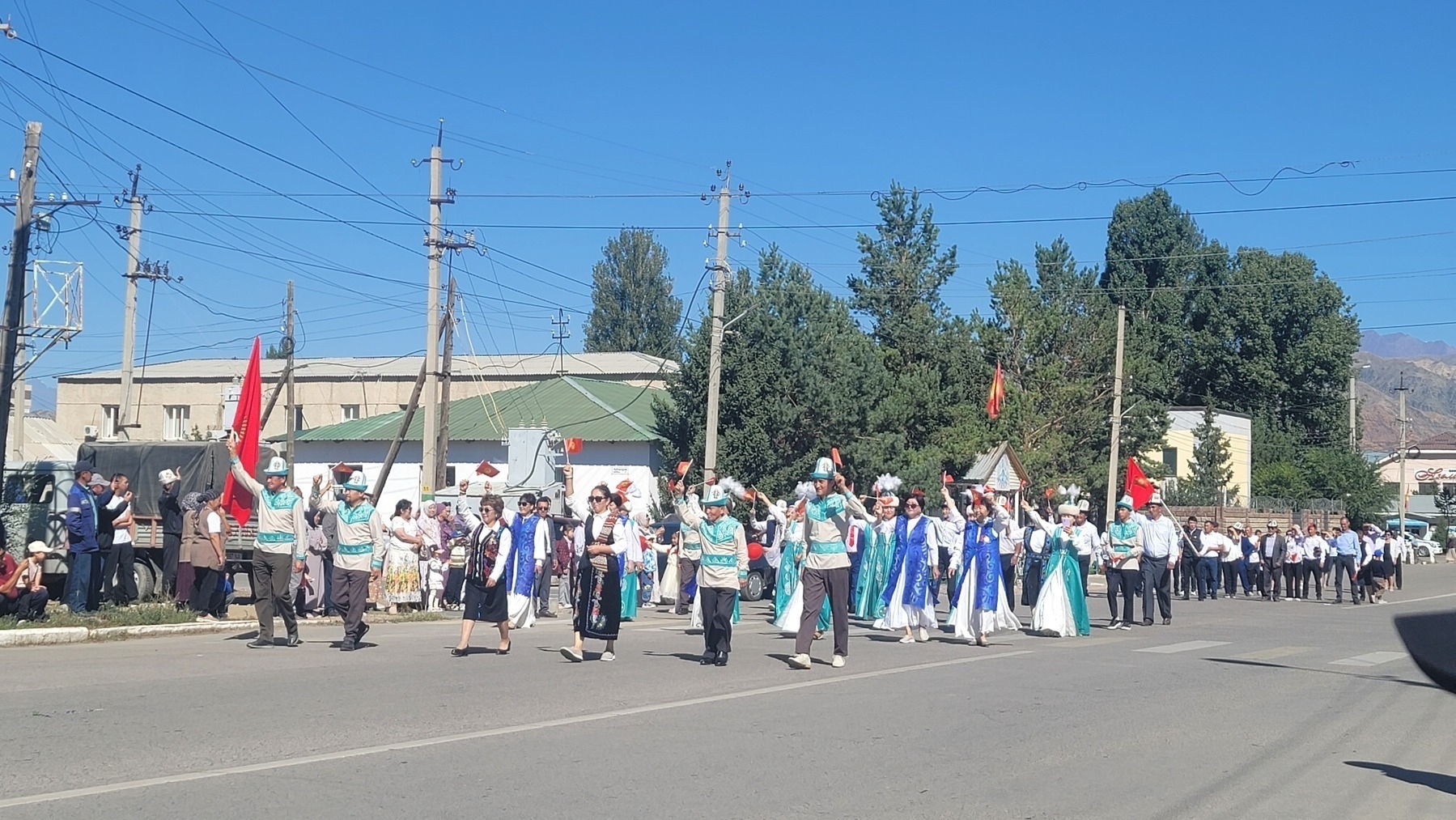 group of people walking down a street wearing traditional clothes and some waving Kyrgyz flags