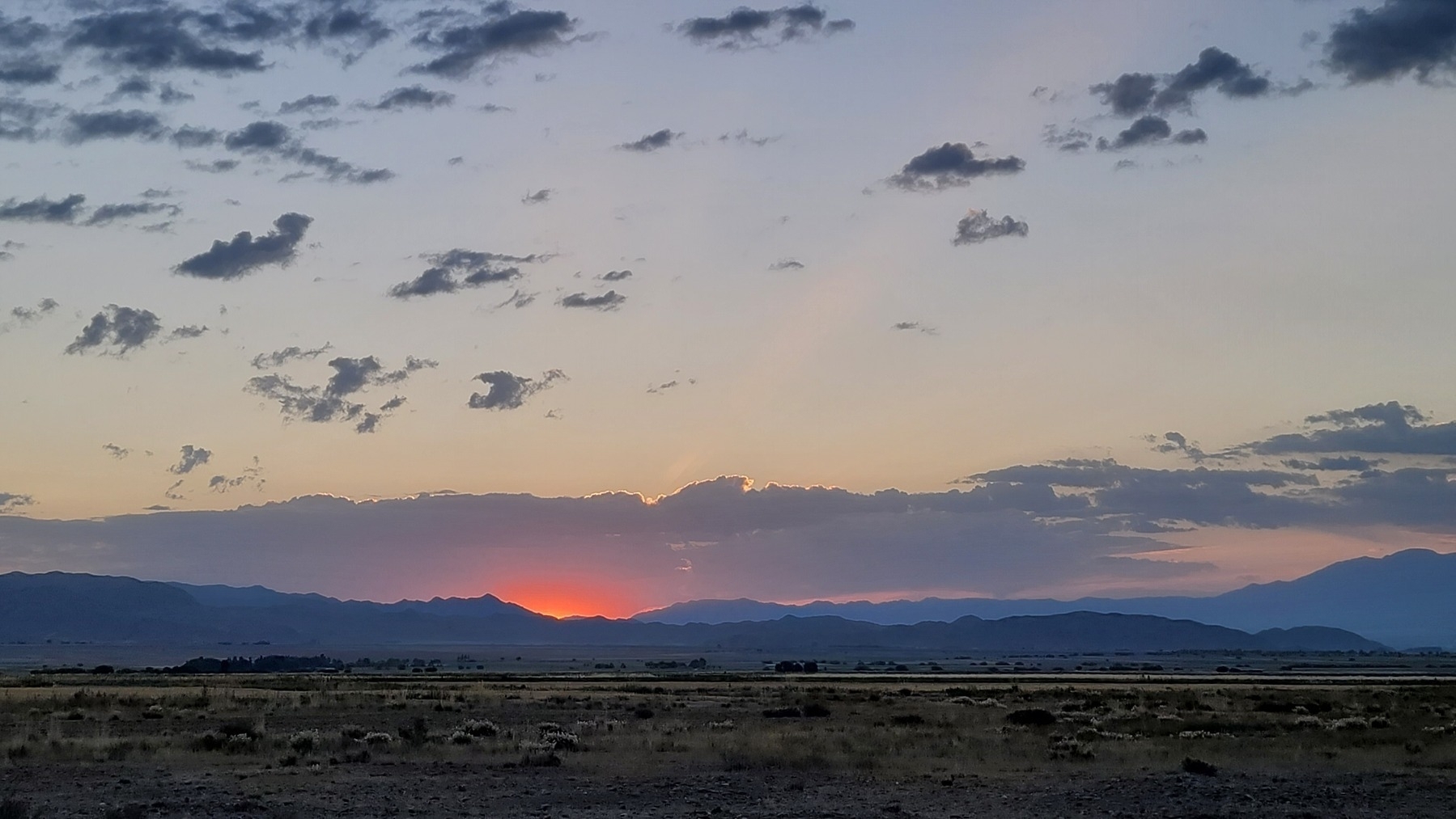 pink/orange light over dark blue mountains and purple/gray cloud over the light from the sun