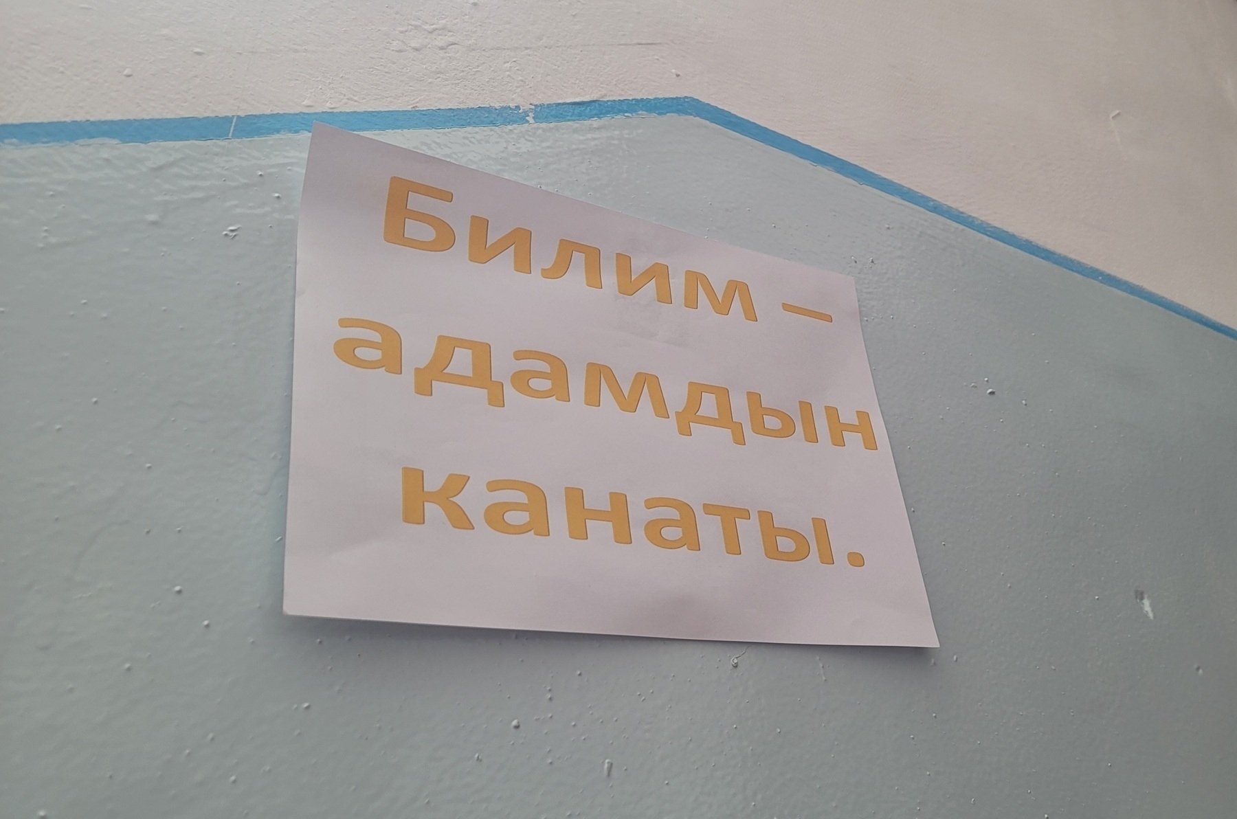 piece of white paper on a school wall printed with a Kyrgyz quote in yellow