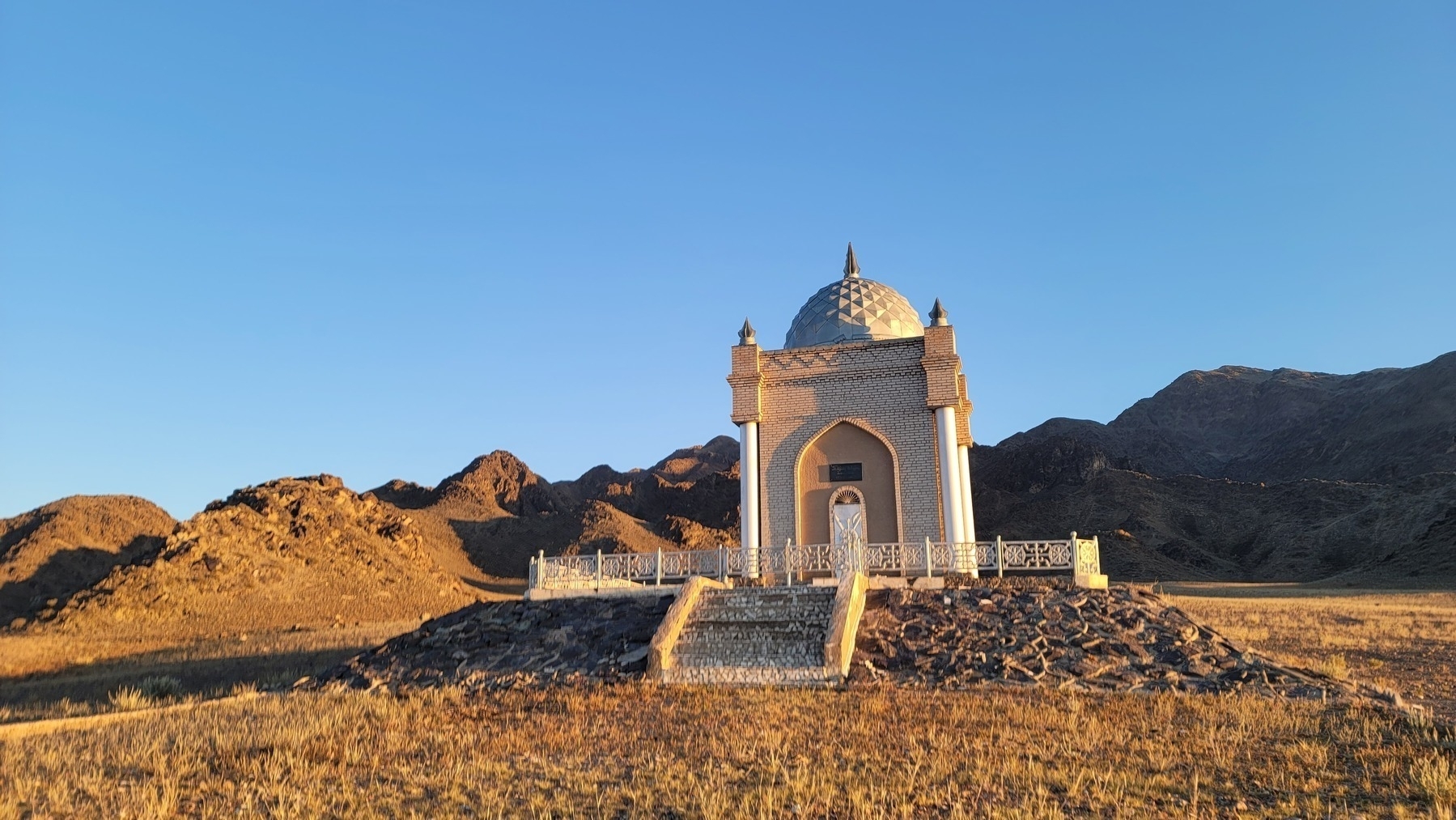 small mausoleum in front of rocky, brown mountains in the morning light