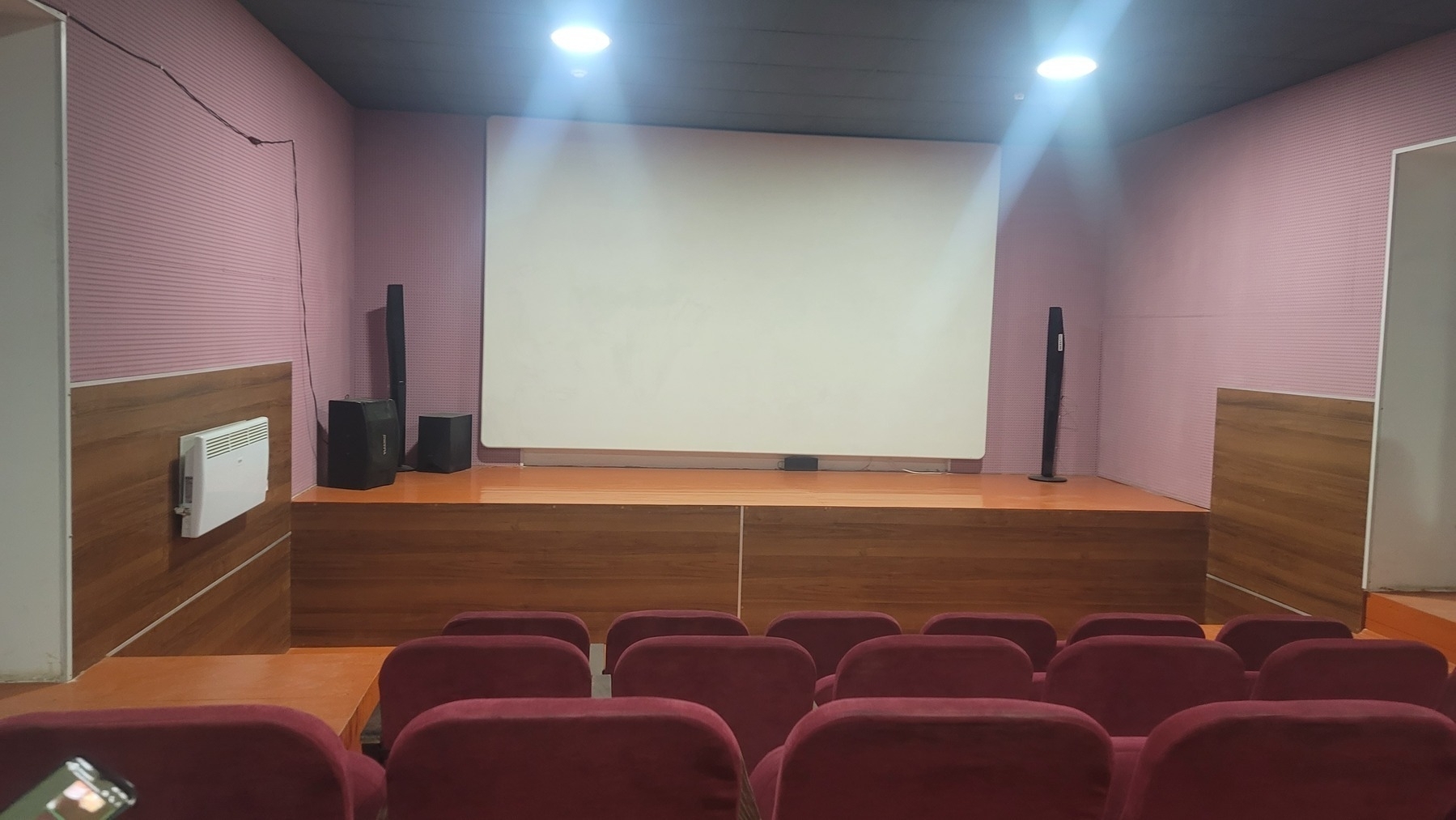 small movie theater room with red theater seats and a screen over a stage at the front of the room 