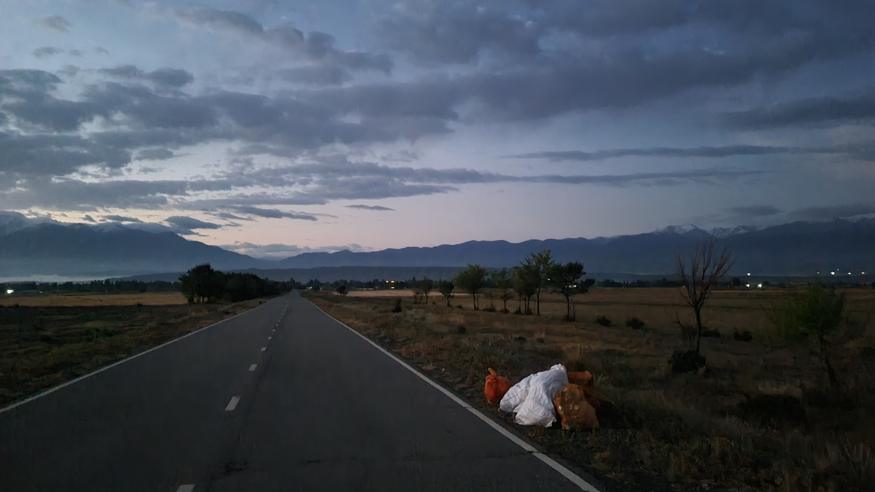 two white and two orange bags along the side of a road on a cloudy morning