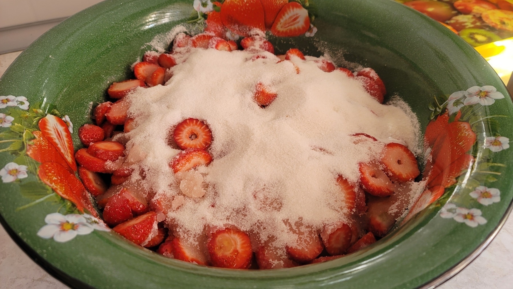 large green bowl with sliced strawberries and sugar