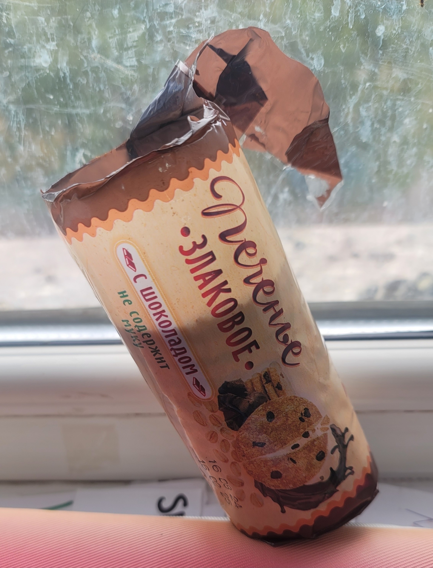 pack of thin, chocolate chip cookies, with almost half of the cookies gone, in front of a window. Russian writing on the package