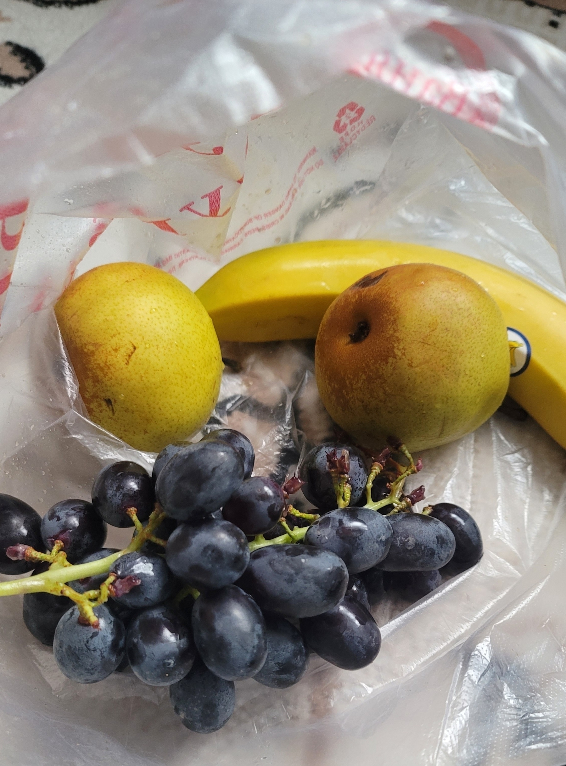 two pears, a banana, and grapes in a plastic bag