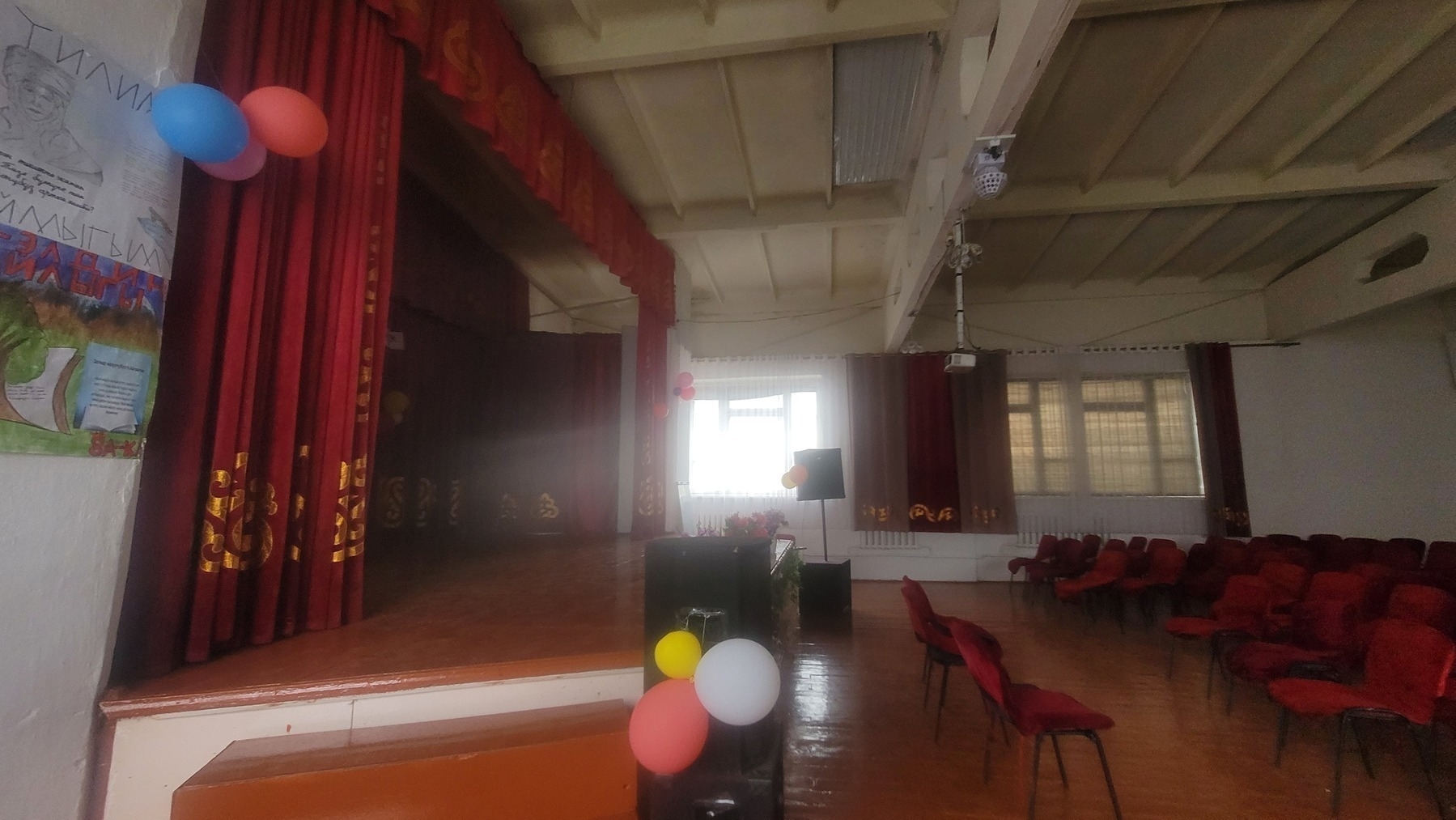 stage with red curtains around it on the left; chairs with red seat covers on the right, facing the stage 