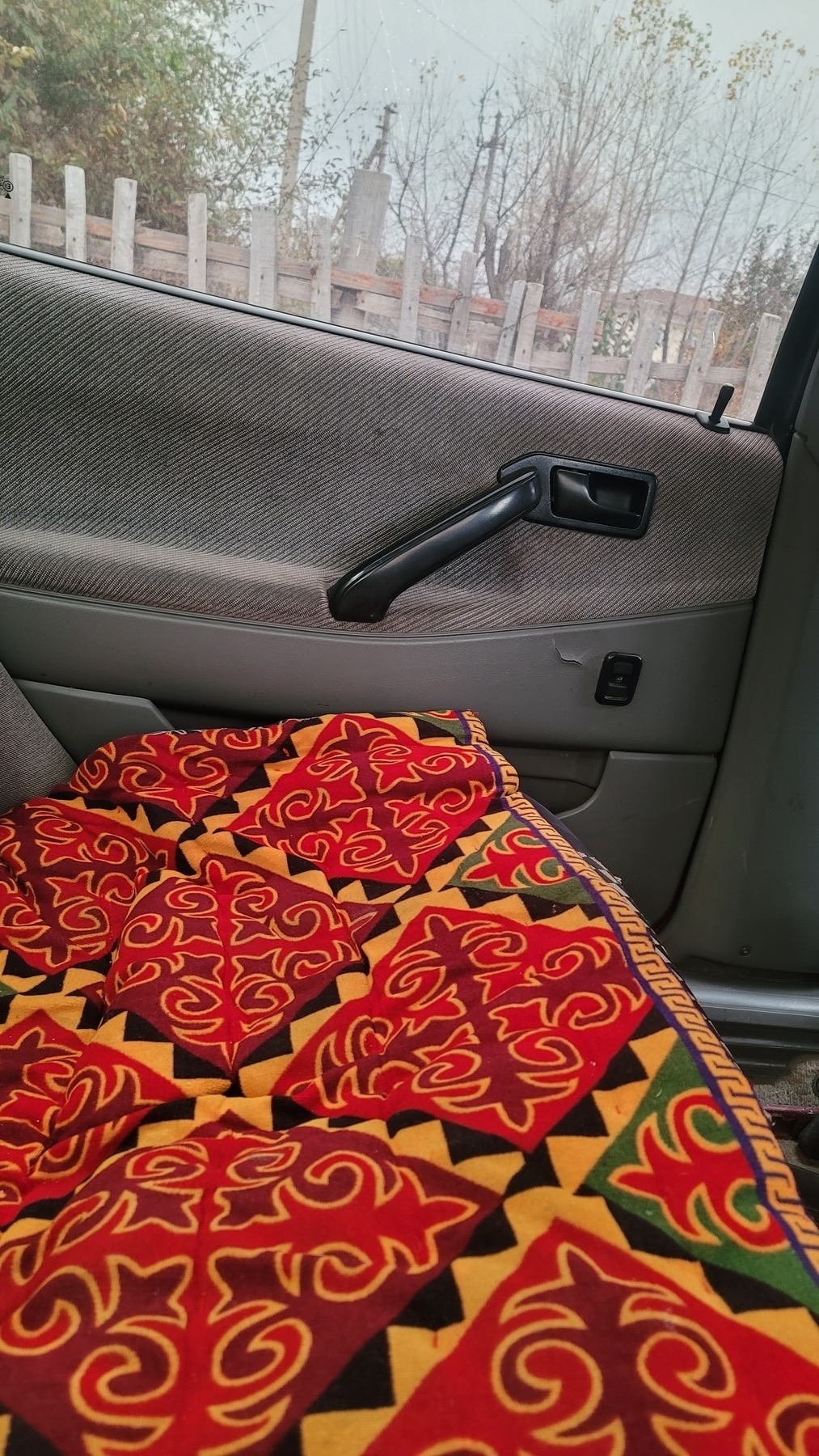 backseat of a car with a thick red/orange pad of geometrical designs (төшөк) on it