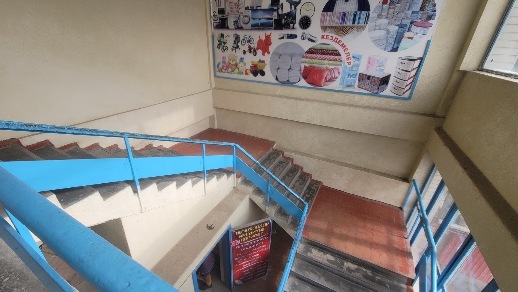 looking down at a stairwell with a blue rail and brown and gray steps. small shop under the stairwell with a banana peel over the shop entrance