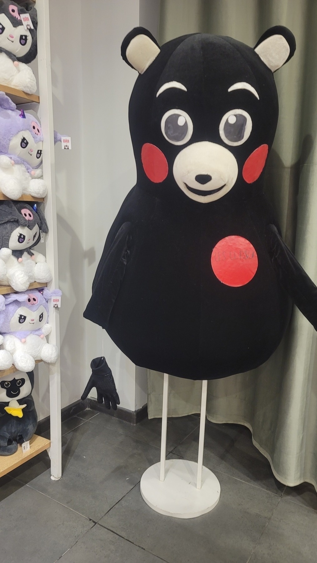 black cartoon bear body and head resembling Kumamon being held up by a base with two small, thin white posts