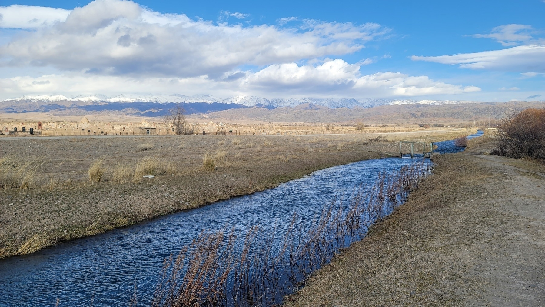 dark blue canal water with ripples on it from the wind; graveyard and mountains in the background