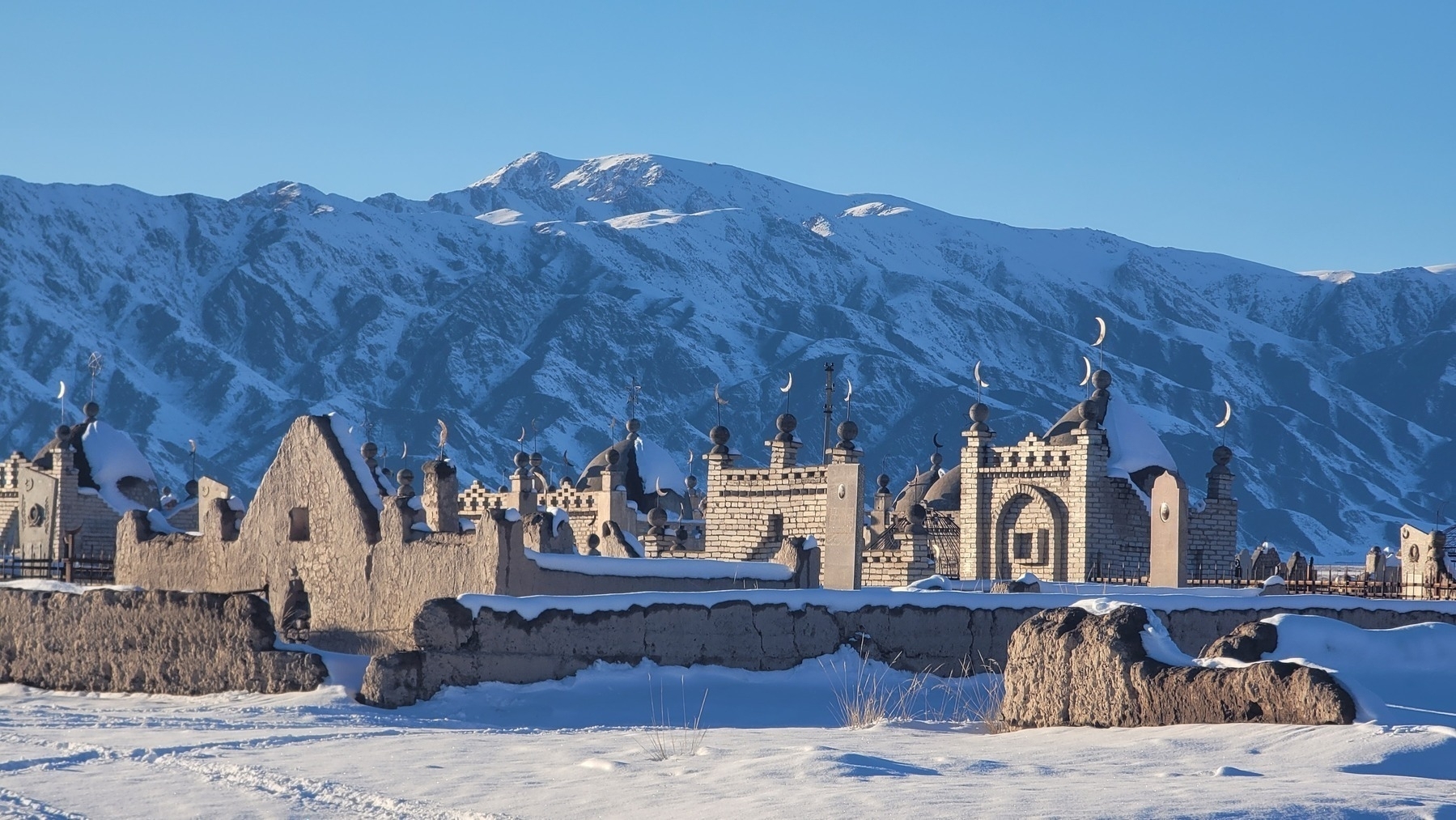 snowy Islamic gravestones in front of snowy mountains