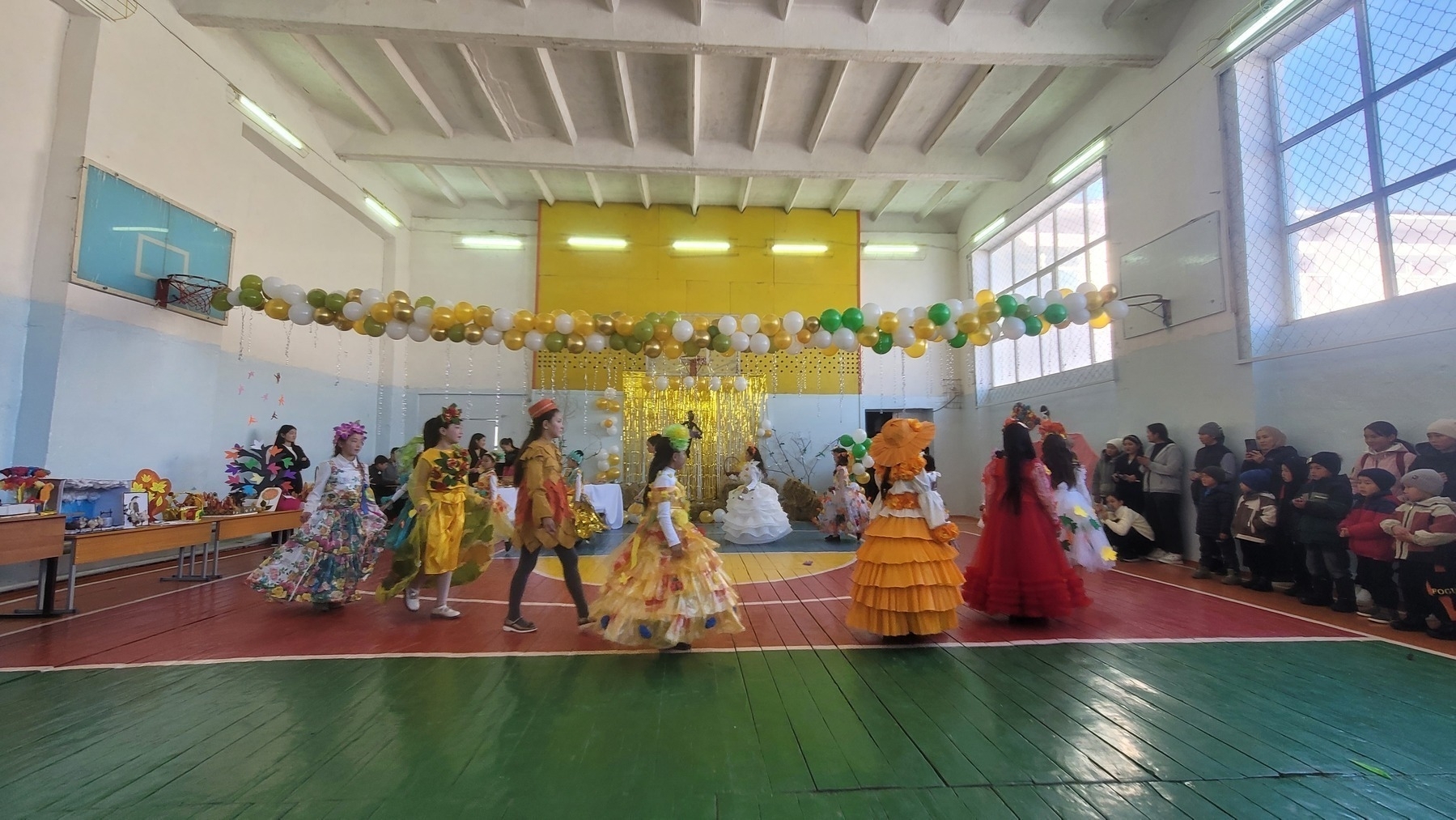 in a school gym, girls with interesting and colorful dresses walking in a circle with spectators on the side