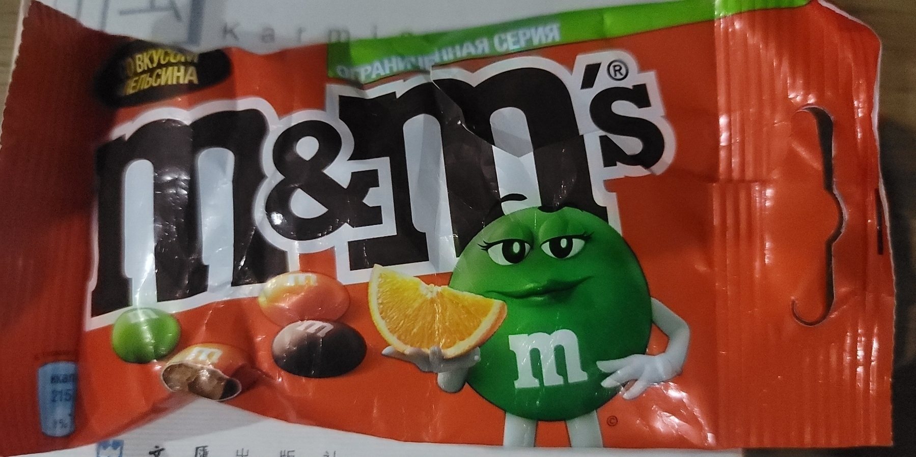 orange packet of orange flavored M&M's, with a green female M&M holding an orange slice