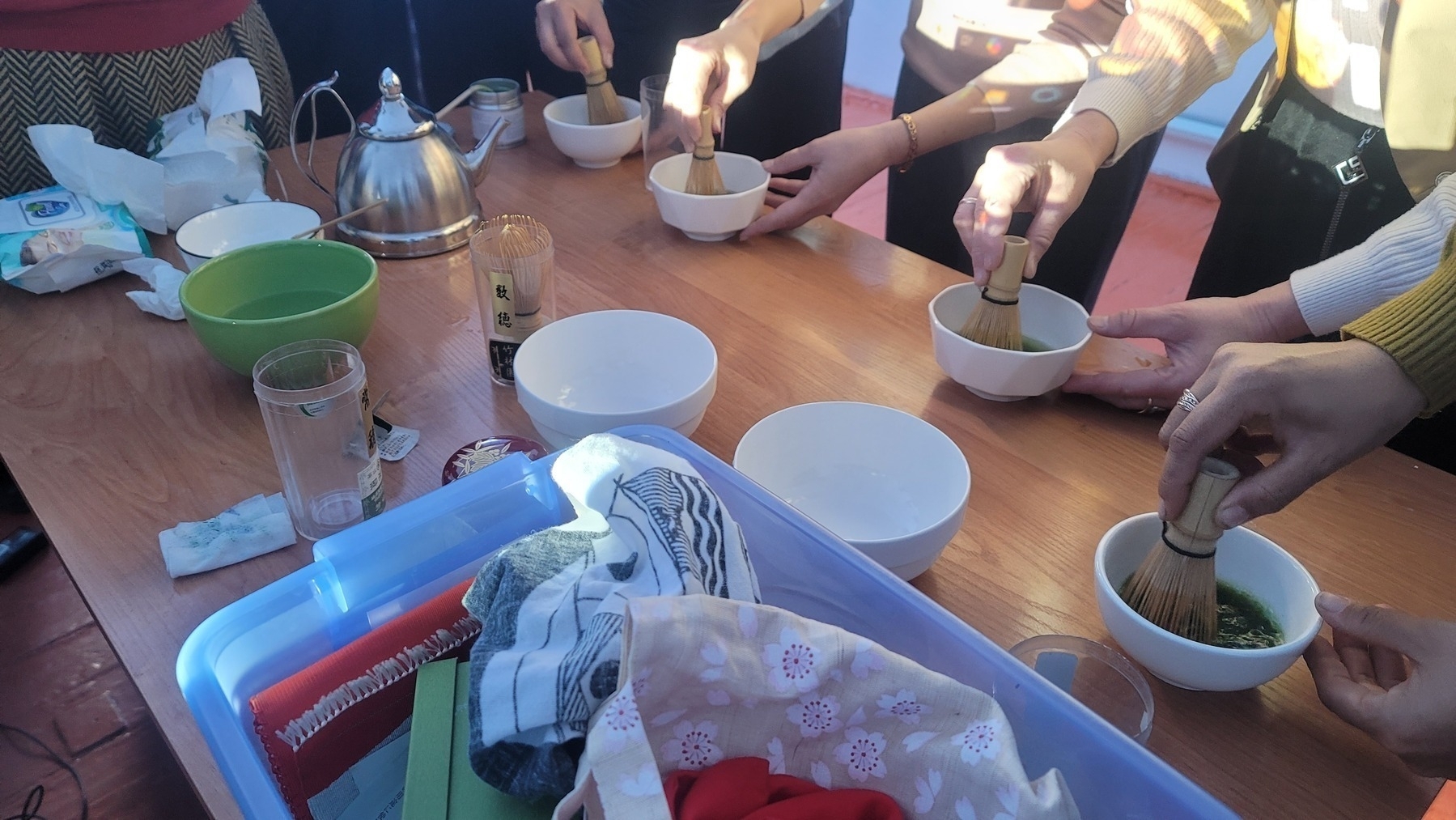 four people mixing matcha powder in hot water for tea with bamboo tea whisks