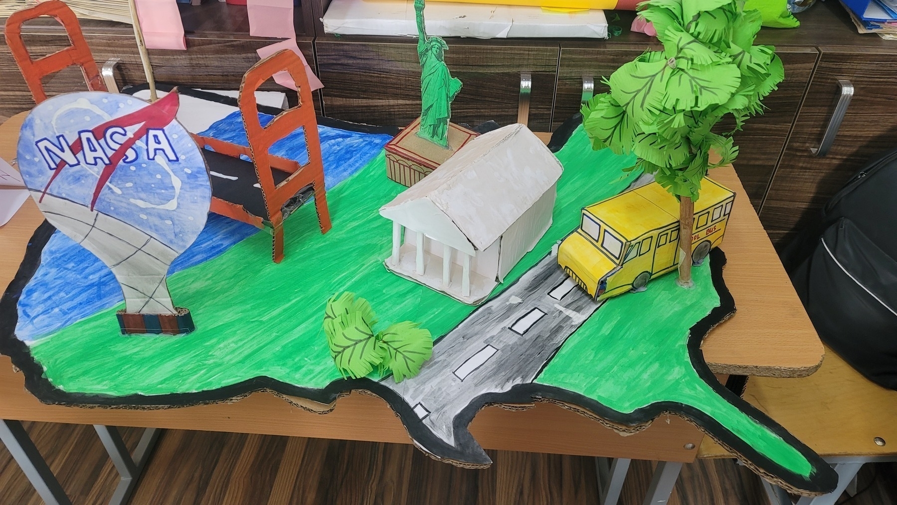 contiguous US made of cardboard, with a school bus, Golden Gate Bridge, White House, NASA, and Statue of Liberty accessories