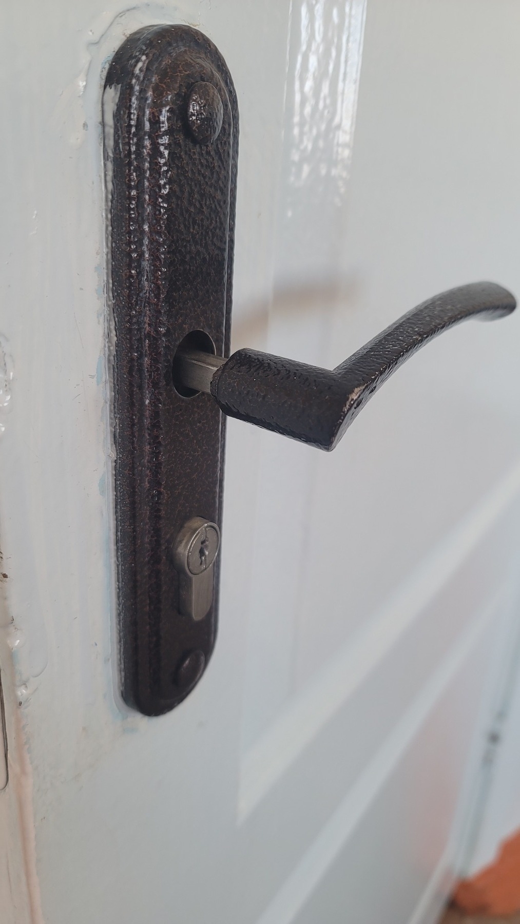 black, metal door knob loosely sitting on a gray, metal bar sticking out from the door