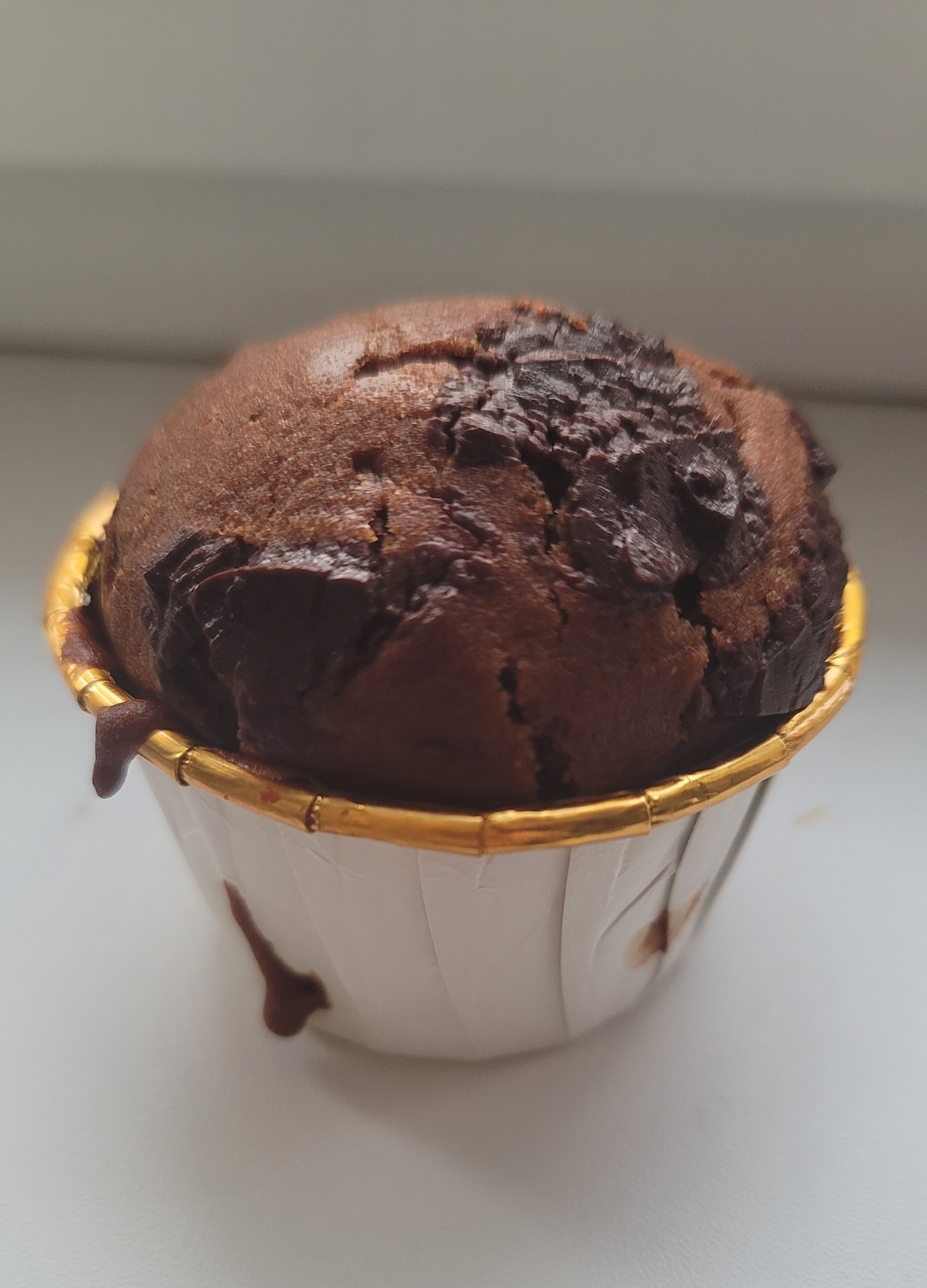 chocolate muffin with chocolate chunks in a white paper muffin cup with a golden rim