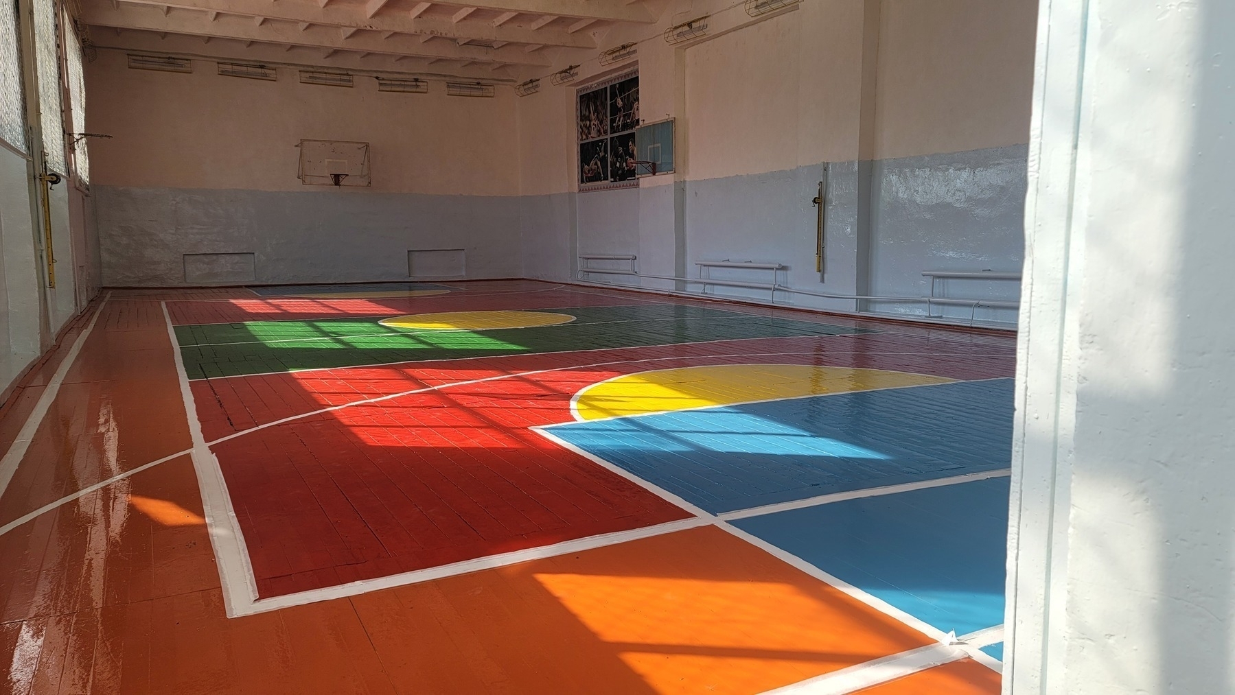 brown-orange gym floor with green, blue, red and yellow painted inside the court/around the court lines