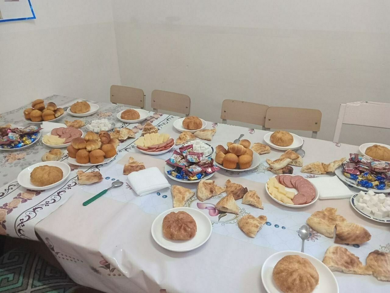 typical Kyrgyz table set up with pastries, candies, cheese and sausage slices, and hoshan (a kind of oily, fried Kyrgyz bun with meat and onions inside) as the main course