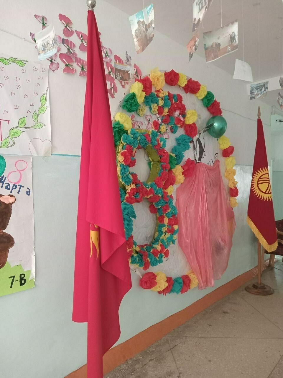 [old] Kyrgyz flags on either side of an "8" made out of colorful paper flowers on the wall. paper pictures of teachers while at the school hanging from the ceiling 