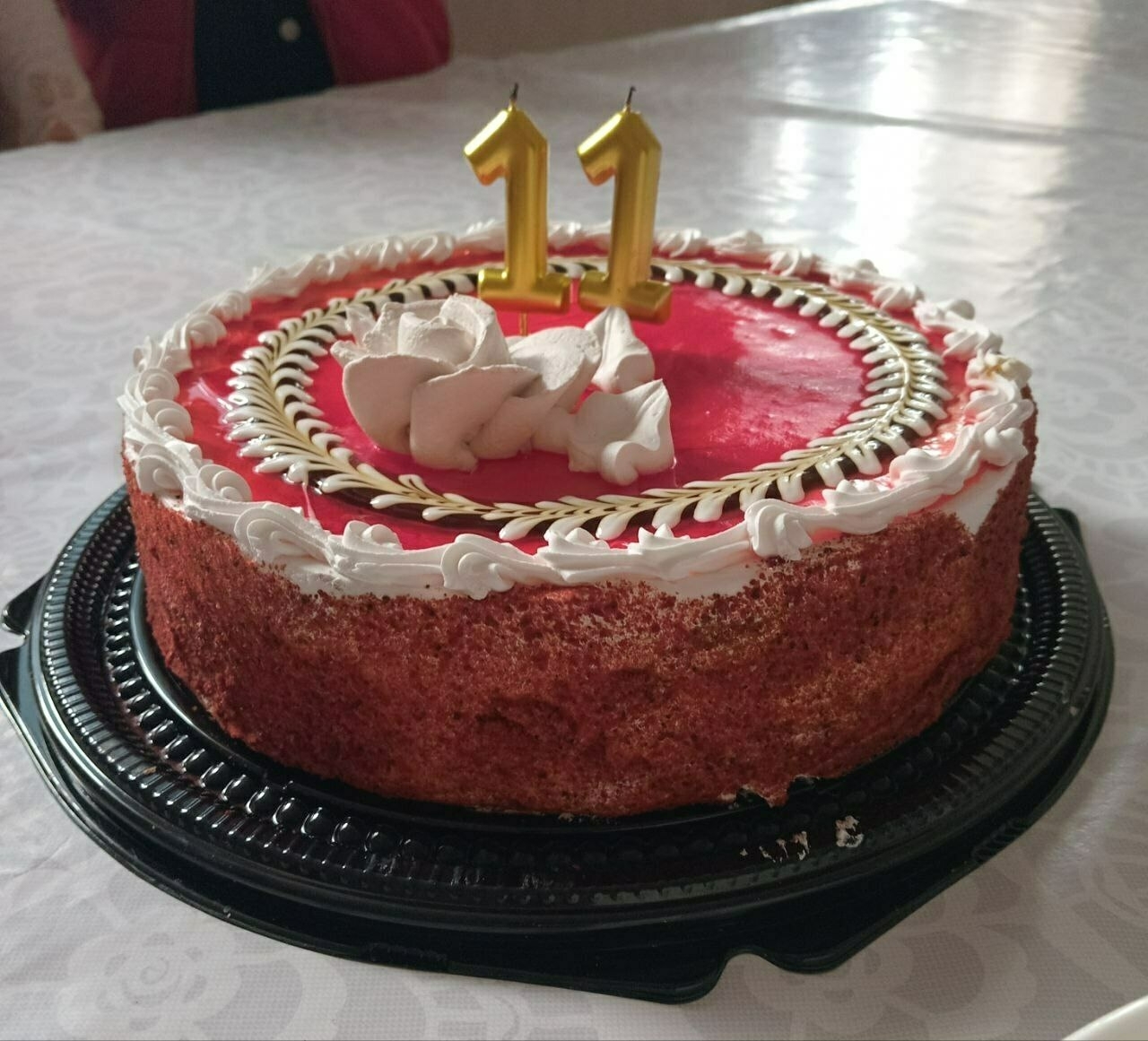 decorated red and white cake on a plastic, black platter with two gold 1 candles on top