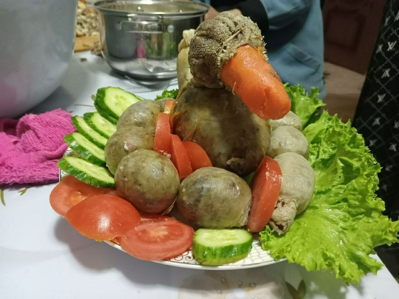 sliced cucumbers and tomatoes around two stacked 'balls' of sausage, with a carrot protruding from the top ball so that the whole thing looks like a duck