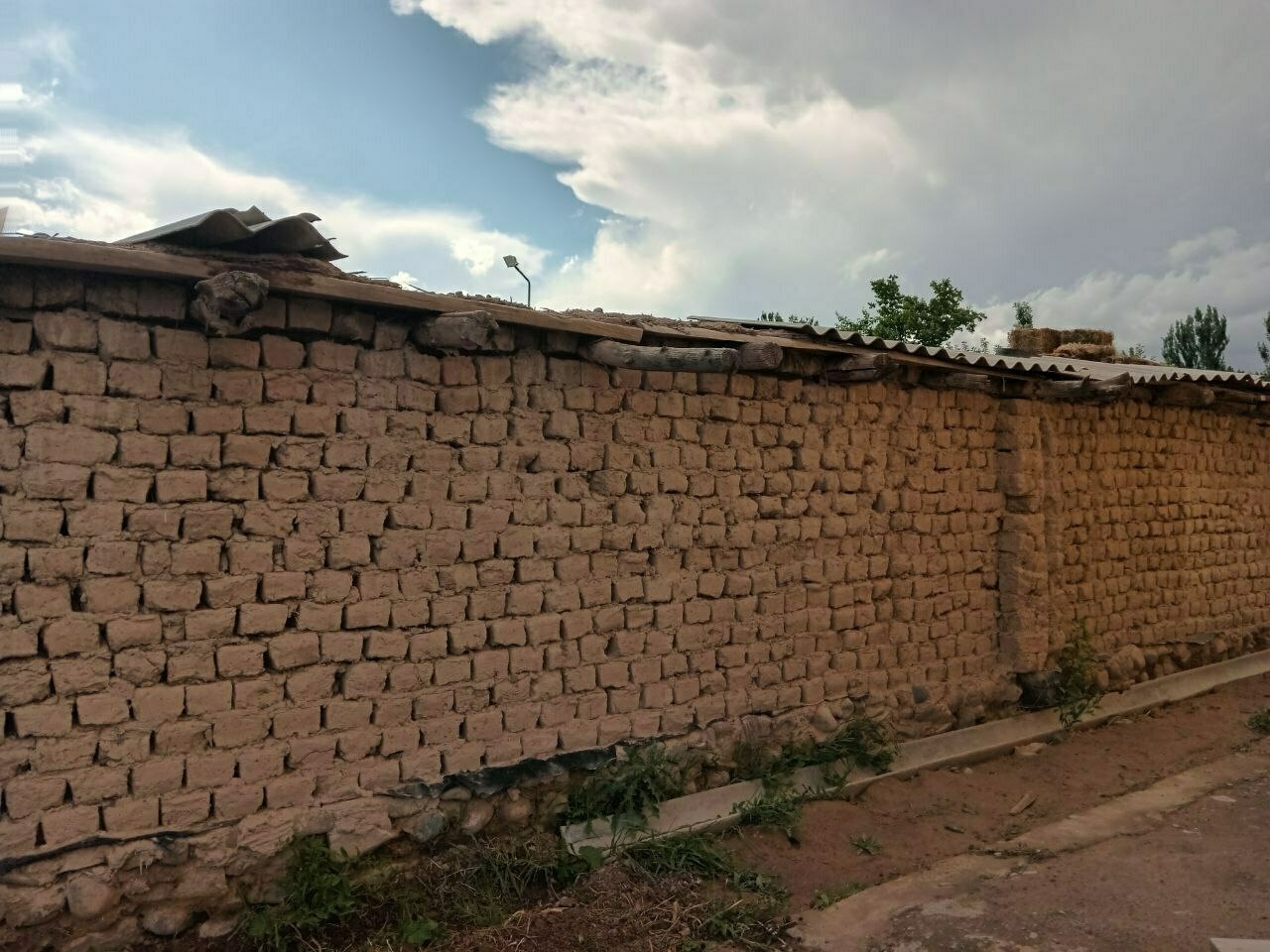 mud brick wall with logs to support wood pieces and large concrete shingle pieces on top