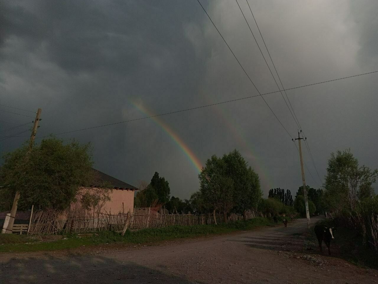 part of a double rainbow visible above a dirt, village road