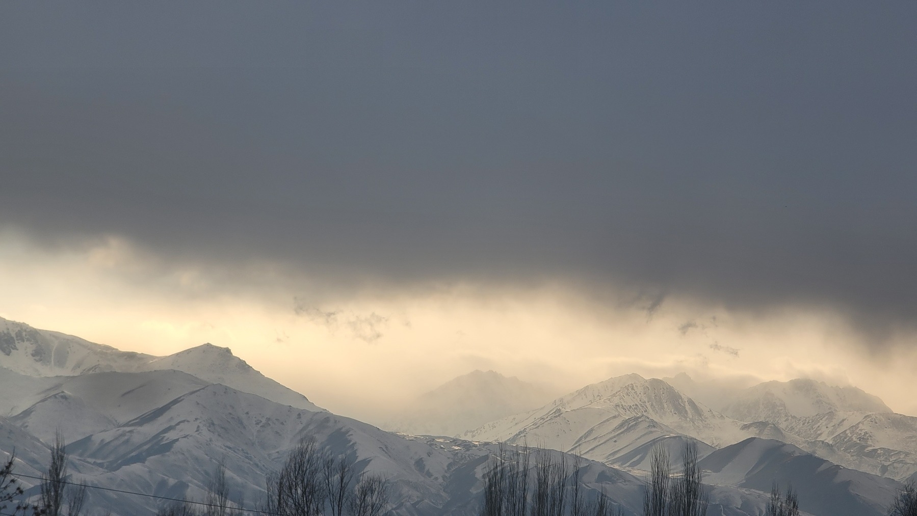 dark cloud shortly before sunset over snowy mountains 