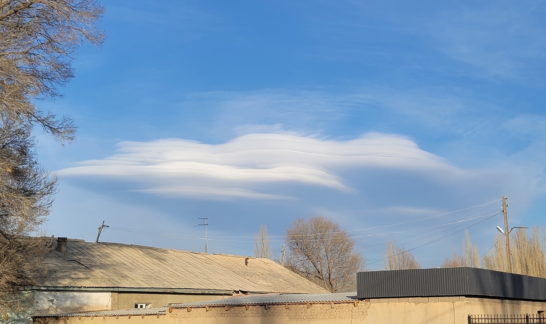 long, smooth, thick white cloud in a blue sky above a house 