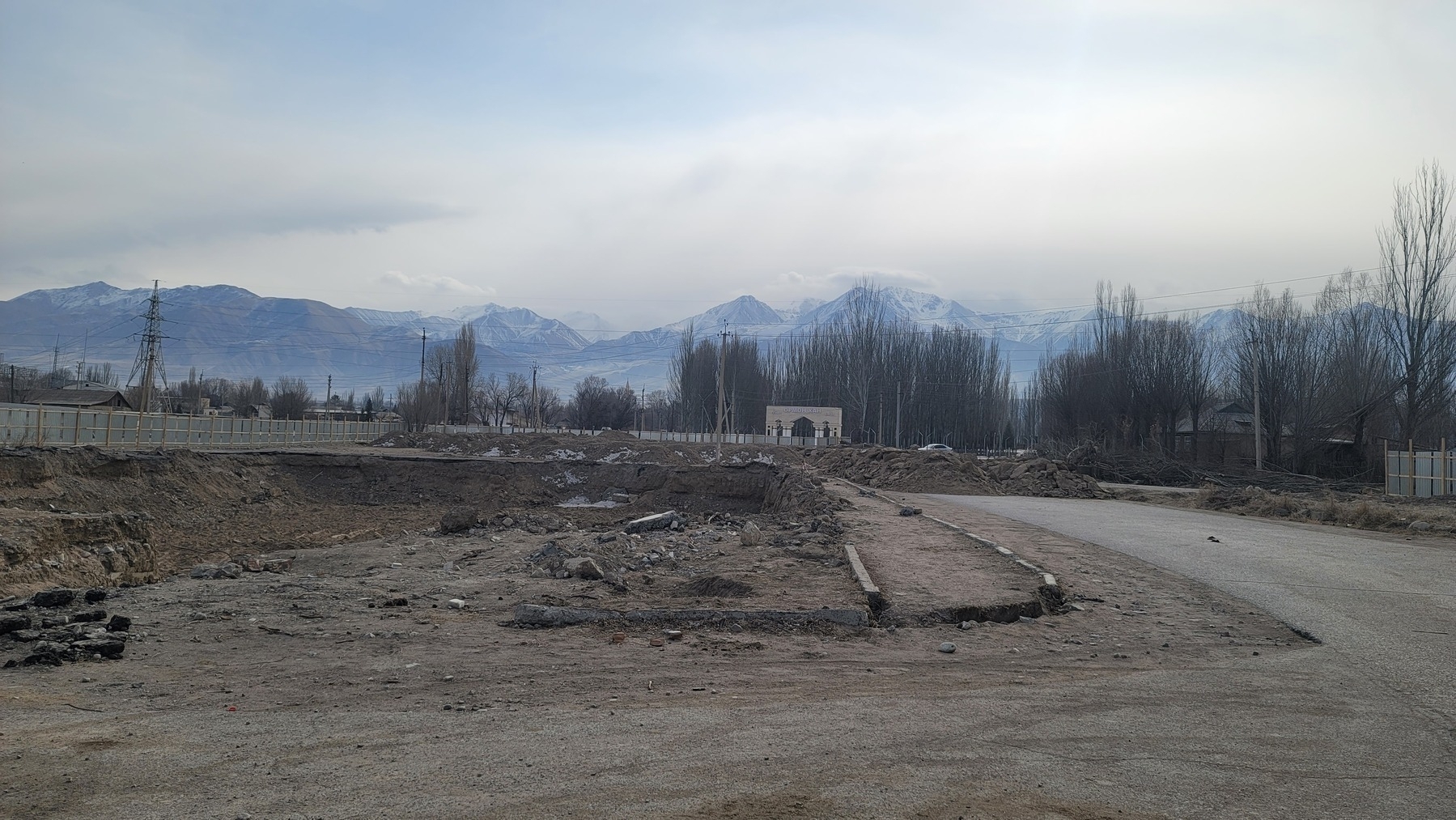 road that ends in a pile of dirt. arch in the distance behind that. mountains in the background