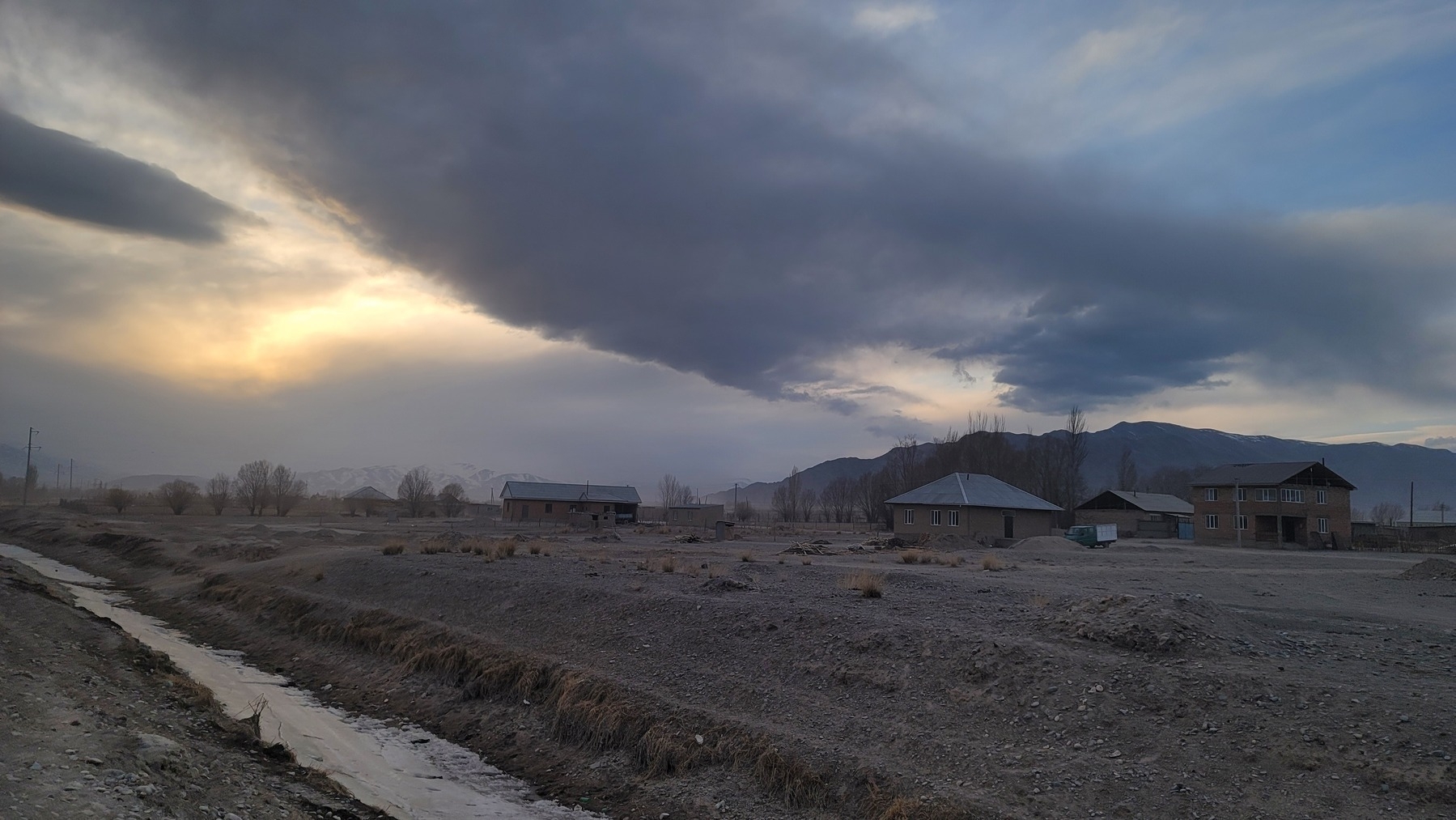 a few village houses around sunset; gray clouds in the sky. mountains in background