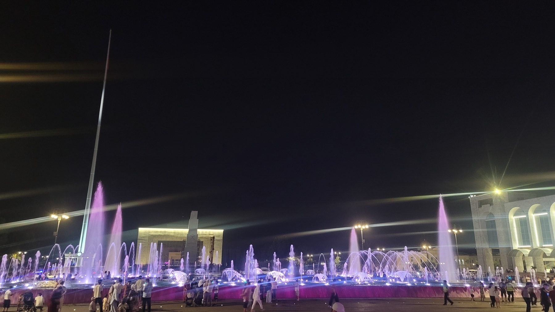 fountains at a square lit-up with purple lights at night