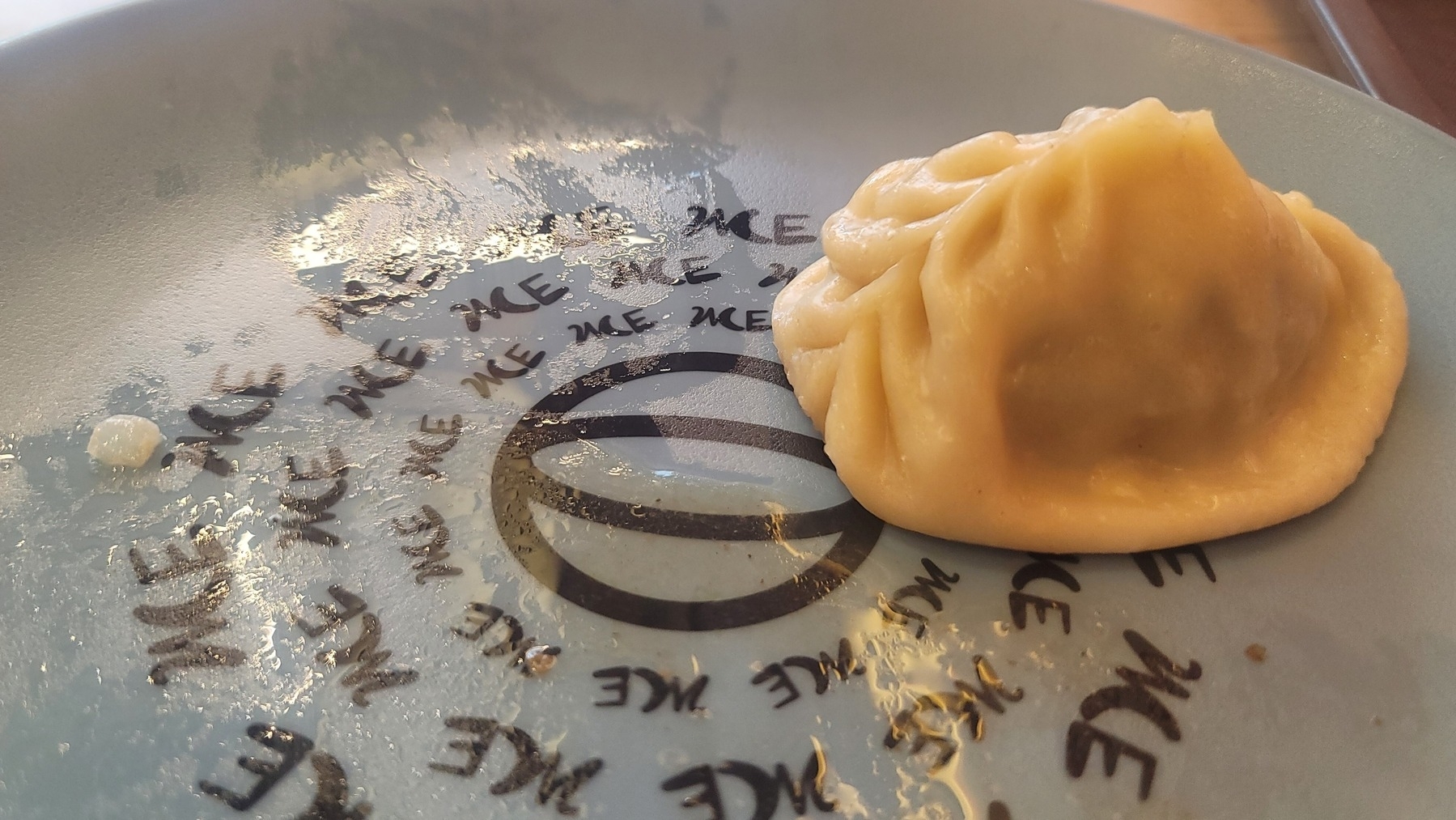 One many (Kyrgyz dumpling) on a plate that has же (eat!) printed on the surface many times around the restaurant logo