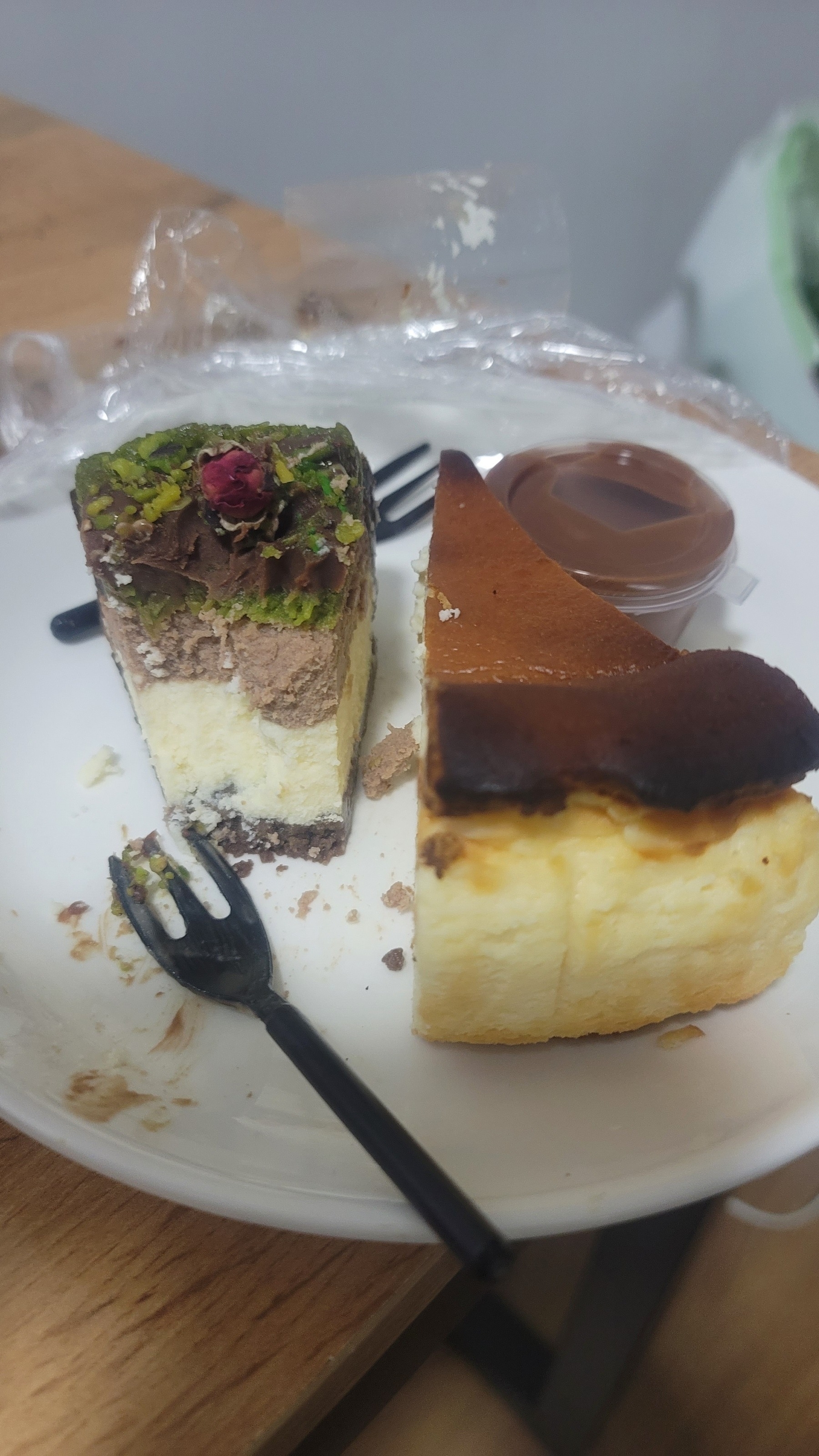 One slice of cheesecake and a half-hearted slice of cheesecake with pistachio, both on a white plate