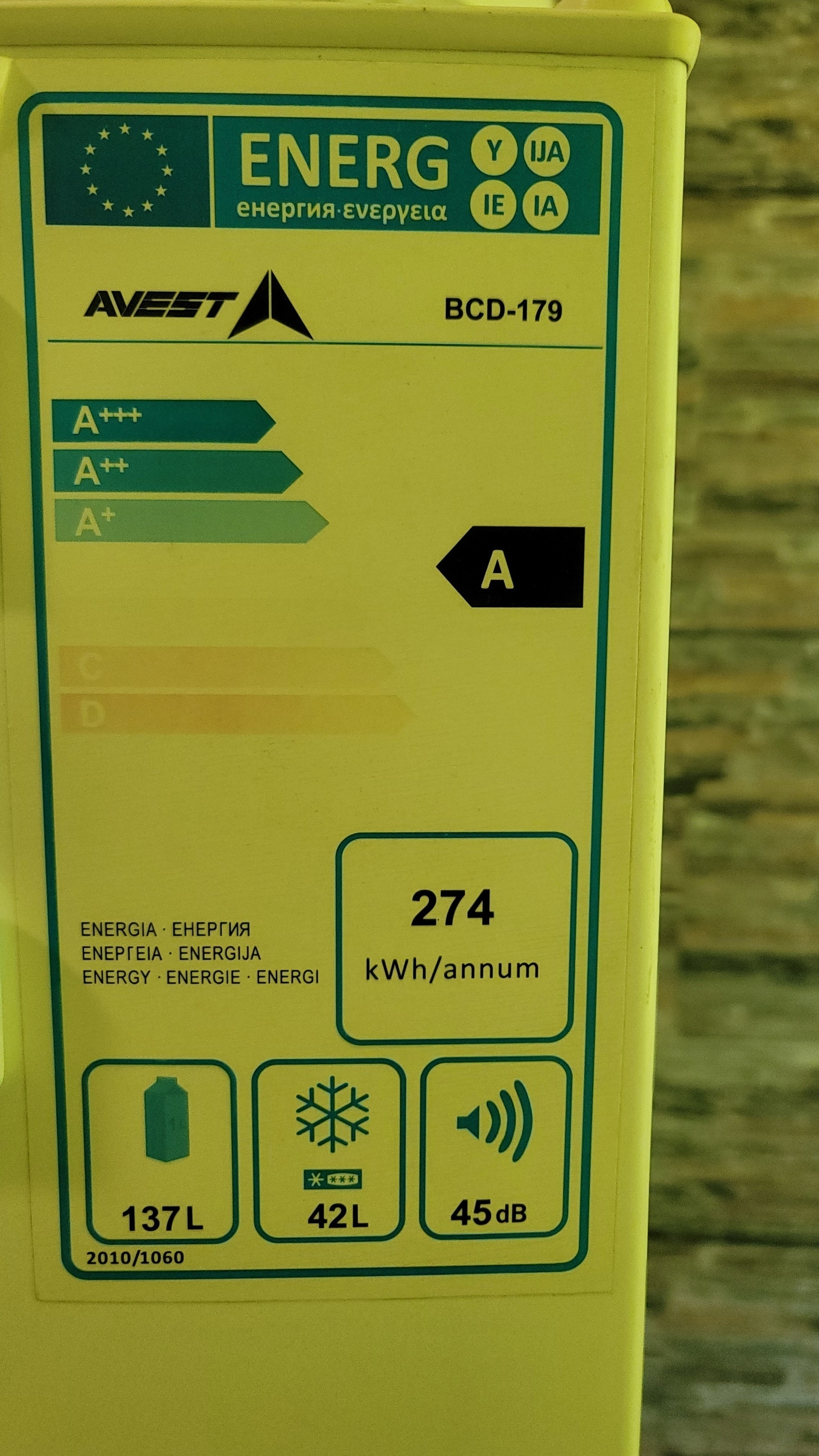 Sticker on a fridge with its specifications in a yellow-ish light, due to light shining into the room through a colored curtain (not pictured)