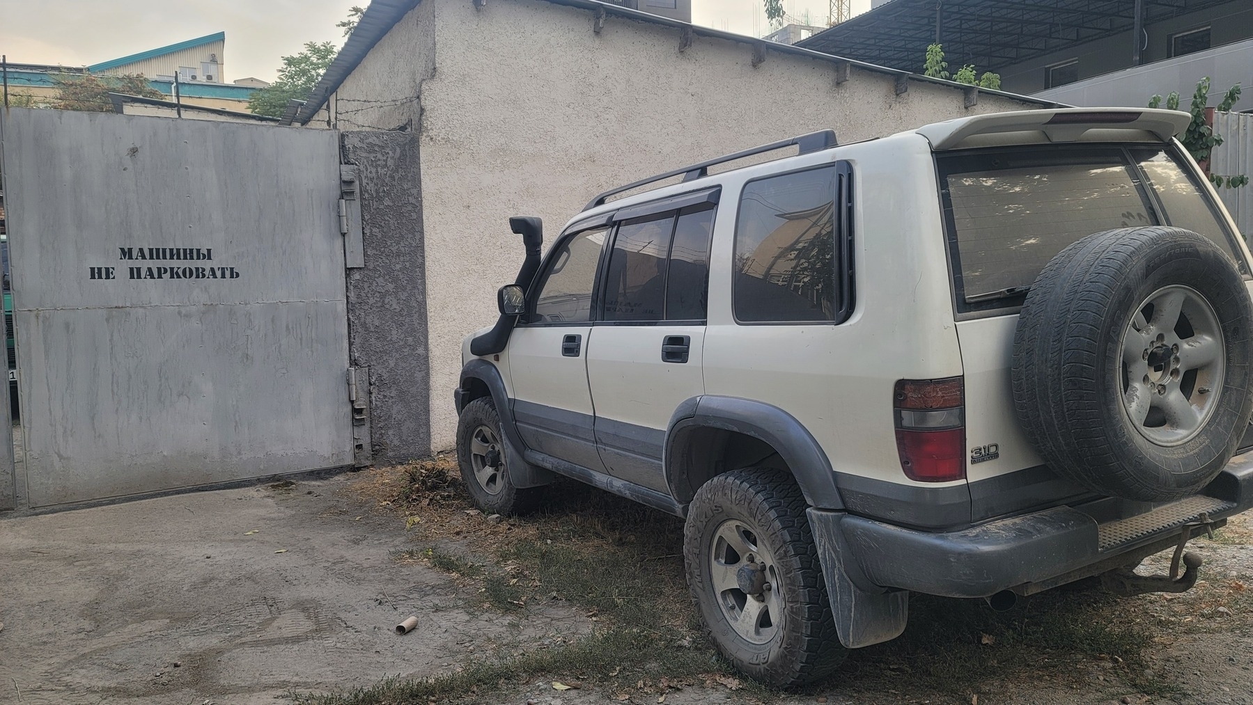 gray and white car next to a metal gate with 'no parking' painted on it