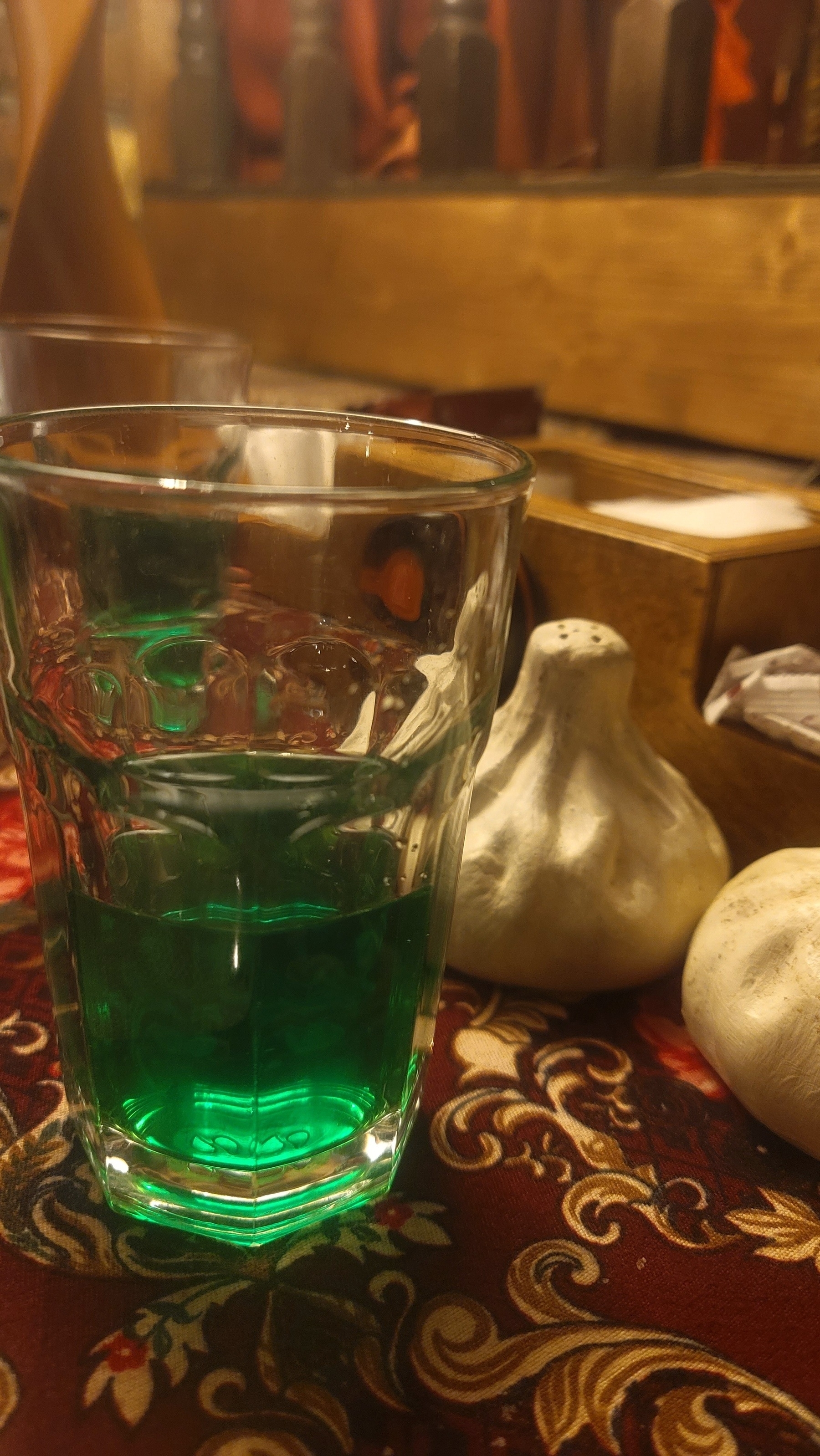 green drink in a clear cup on top of a dark red patterned table fabric, next to khinkali (Georgian dumpling) shaped salt and pepper shakers